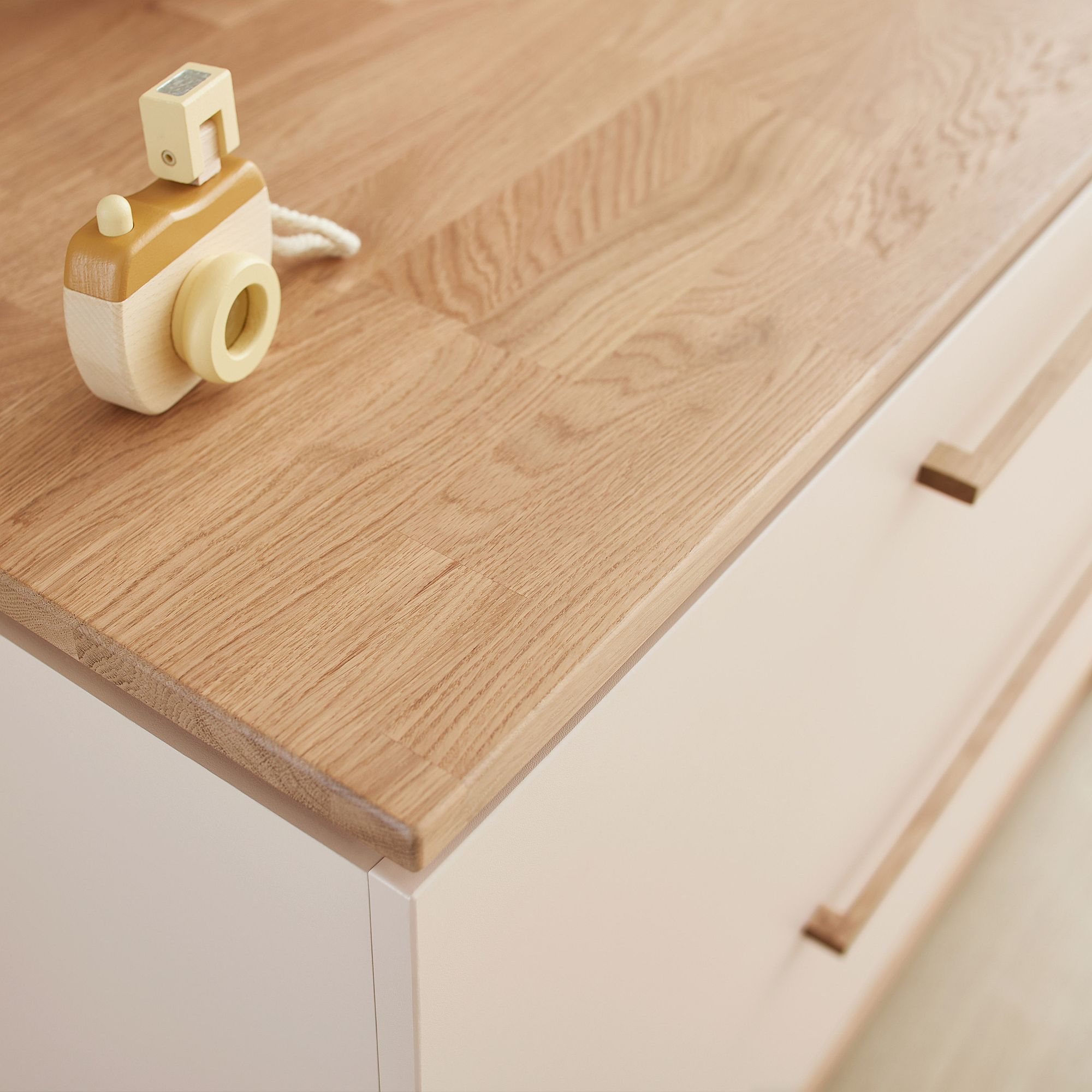 Spielzeugkamera aus Holz auf einer hellen Holzkommode mit minimalistischen Griffen.