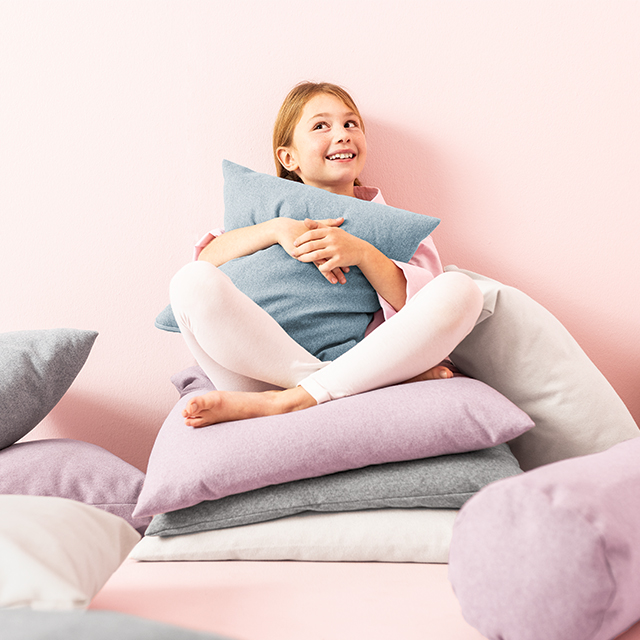 Smiling girl hugging a pillow while sitting on a pile of cushions.