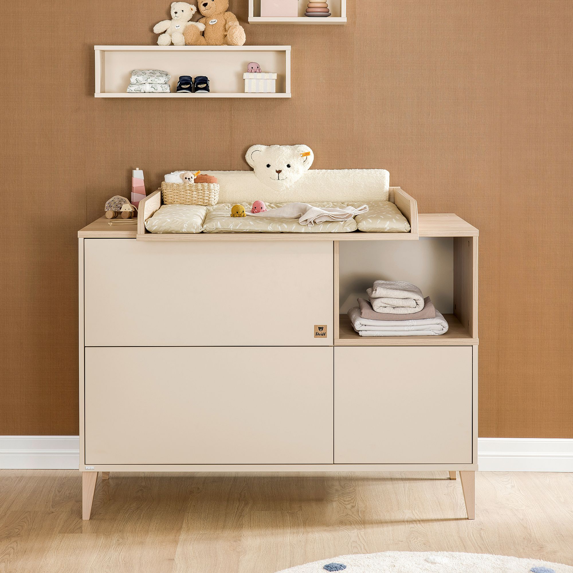 Beigefarbener Wickeltisch mit Teddybär-Kissen und Babyutensilien obenauf.