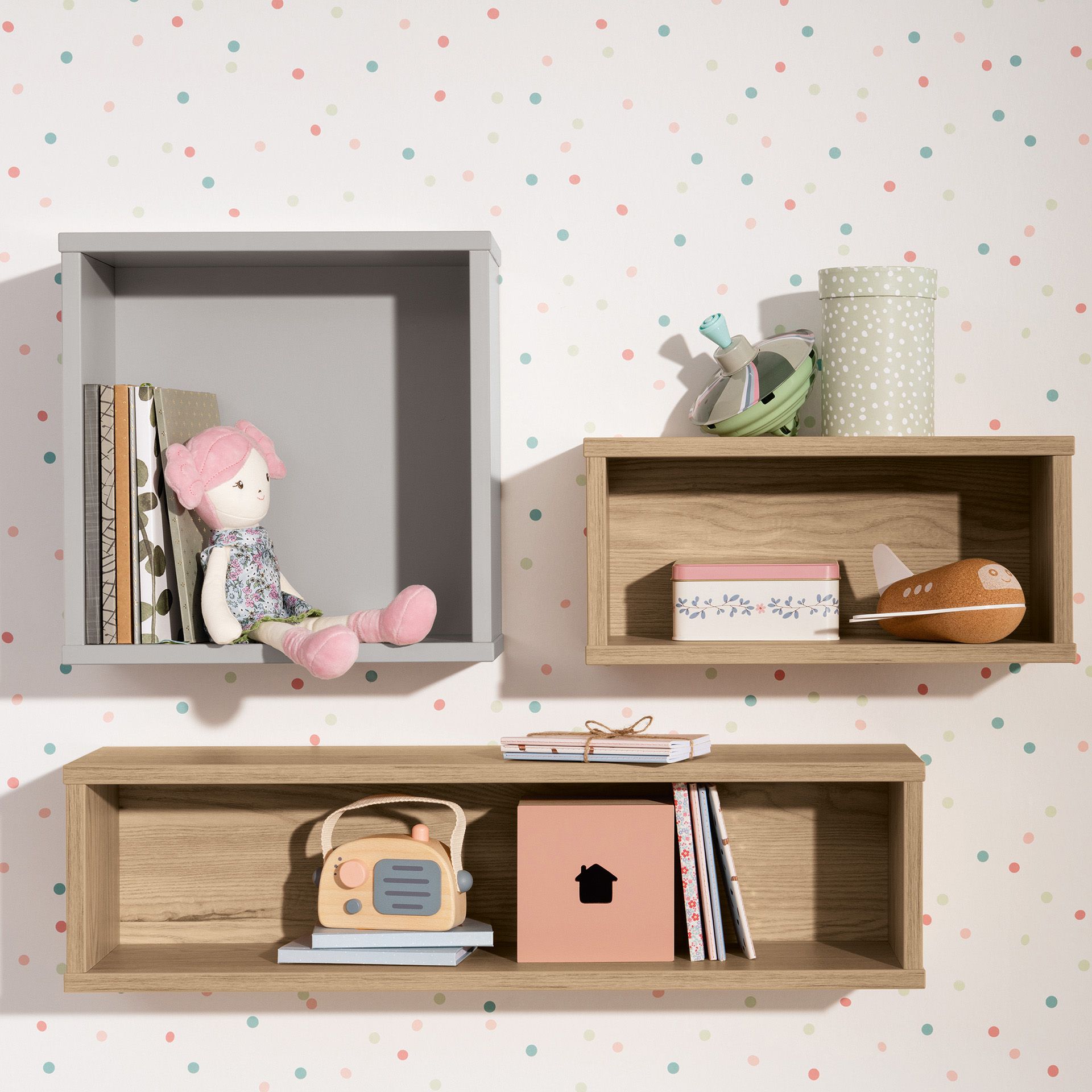 Wandregal  Wandbox  quadratisch in Kieselgrau Wandregale mit Büchern, Spielzeug und Dekoration vor einer pastellfarbenen Wand mit Tupfen.