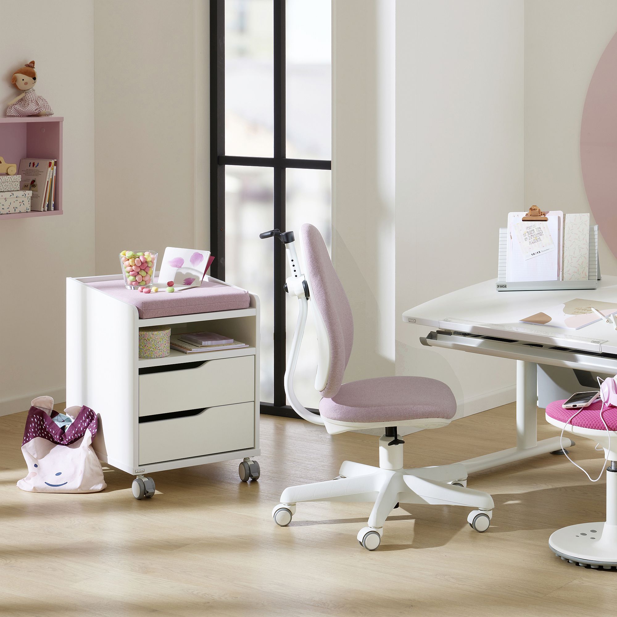 Modern study area with a pink chair, desk, storage unit, and kids accessories.