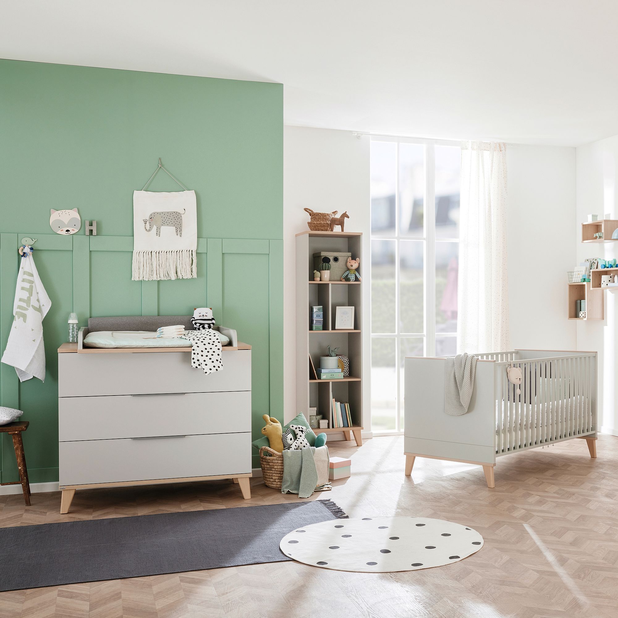 Modern nursery with a crib, dresser, toys, and pastel green accent wall.
