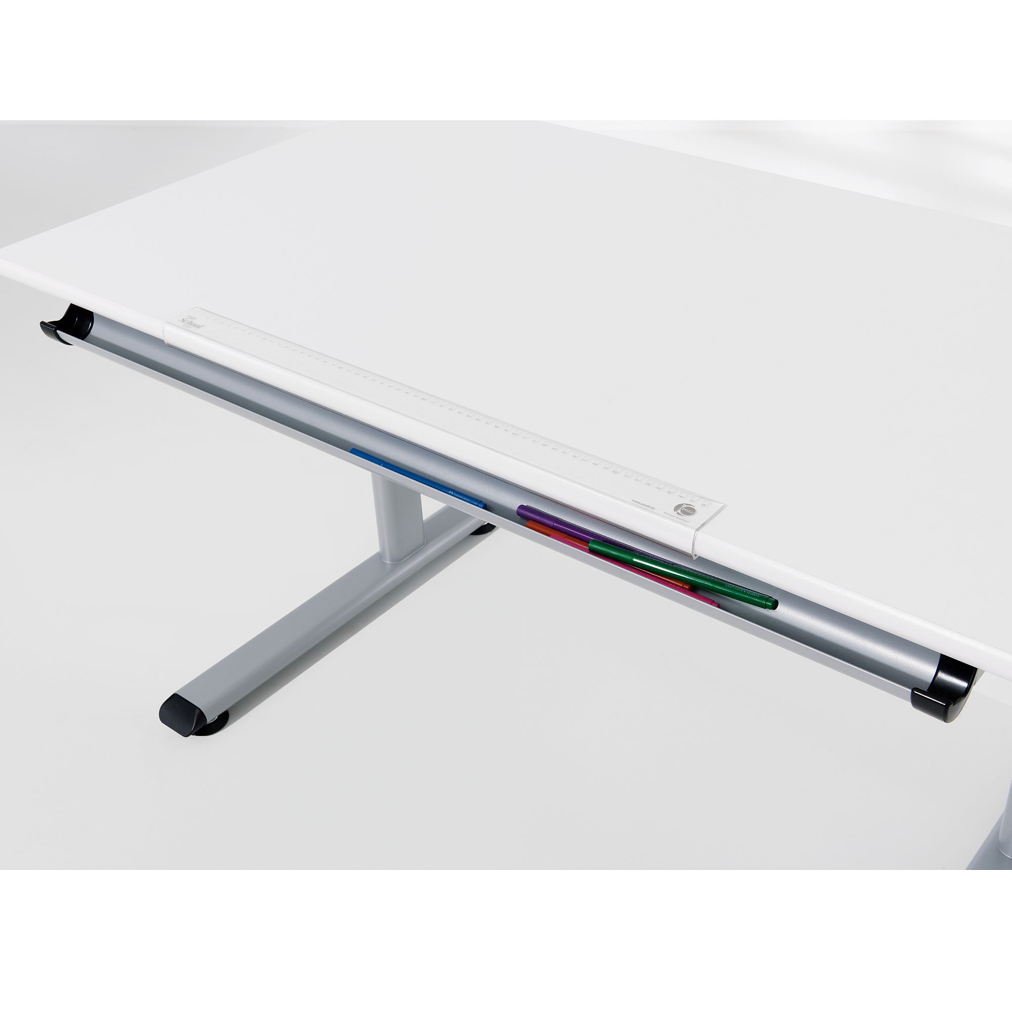 Weißer Schreibtisch mit Lineal und Buntstiften, die in einer Rille an der Kante liegen.