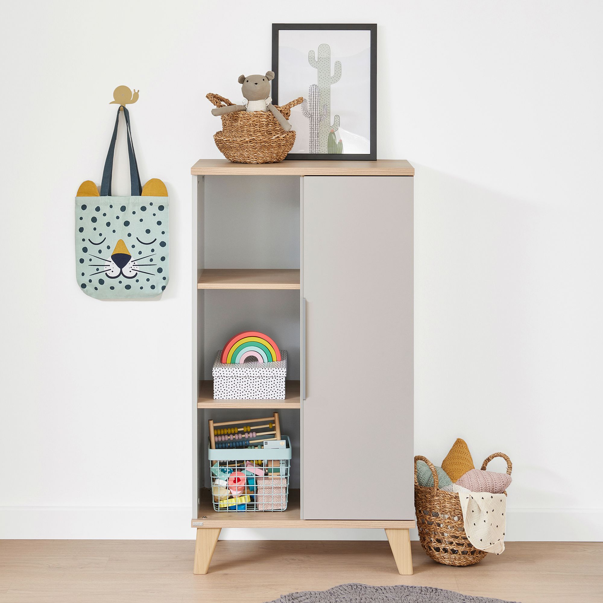 Hoher grauer Schrank mit Spielzeug, Büchern und Körben in einem Kinderzimmer.