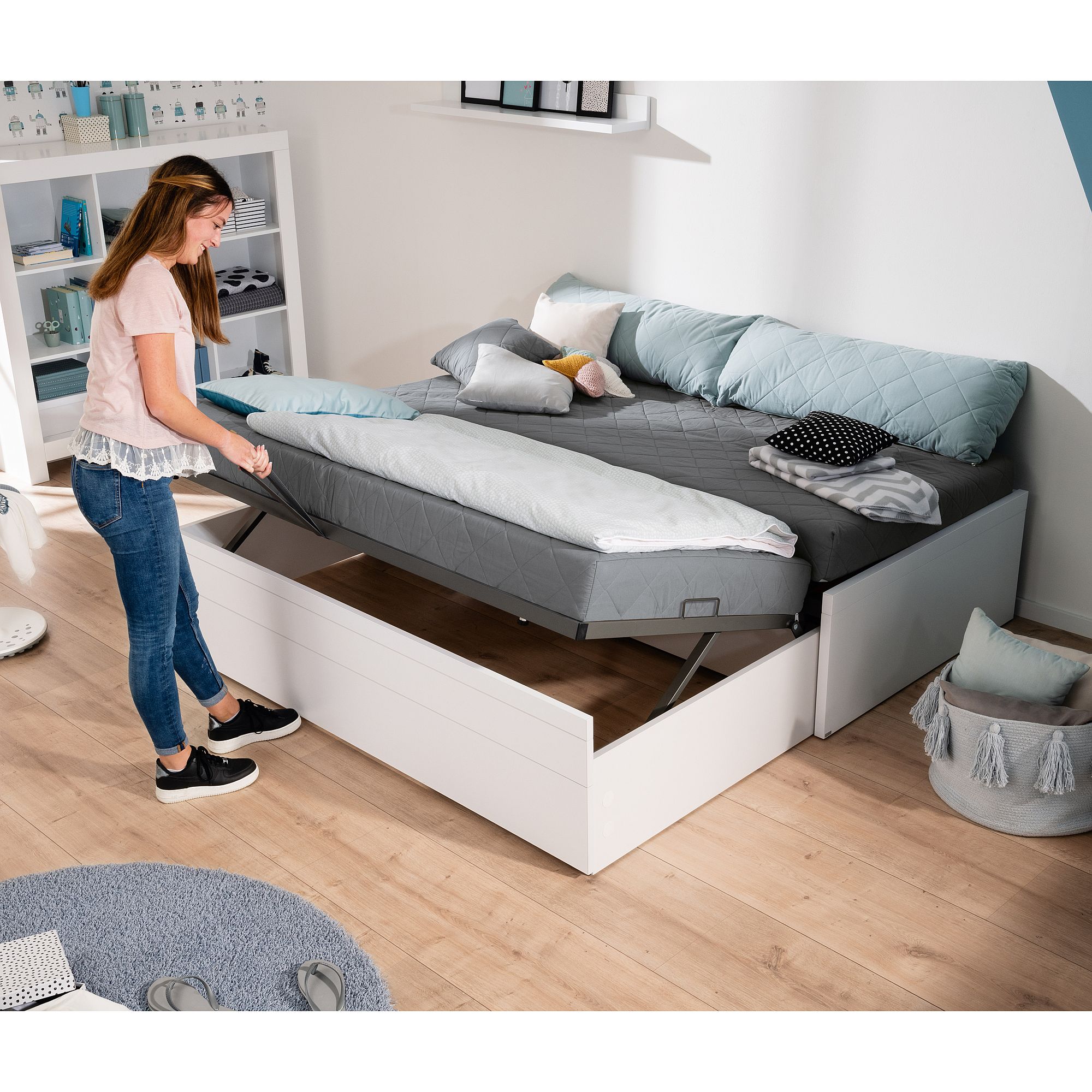 Frau hebt Matratze auf einem weißen Stauraumbett in einem modernen, aufgeräumten Schlafzimmer.