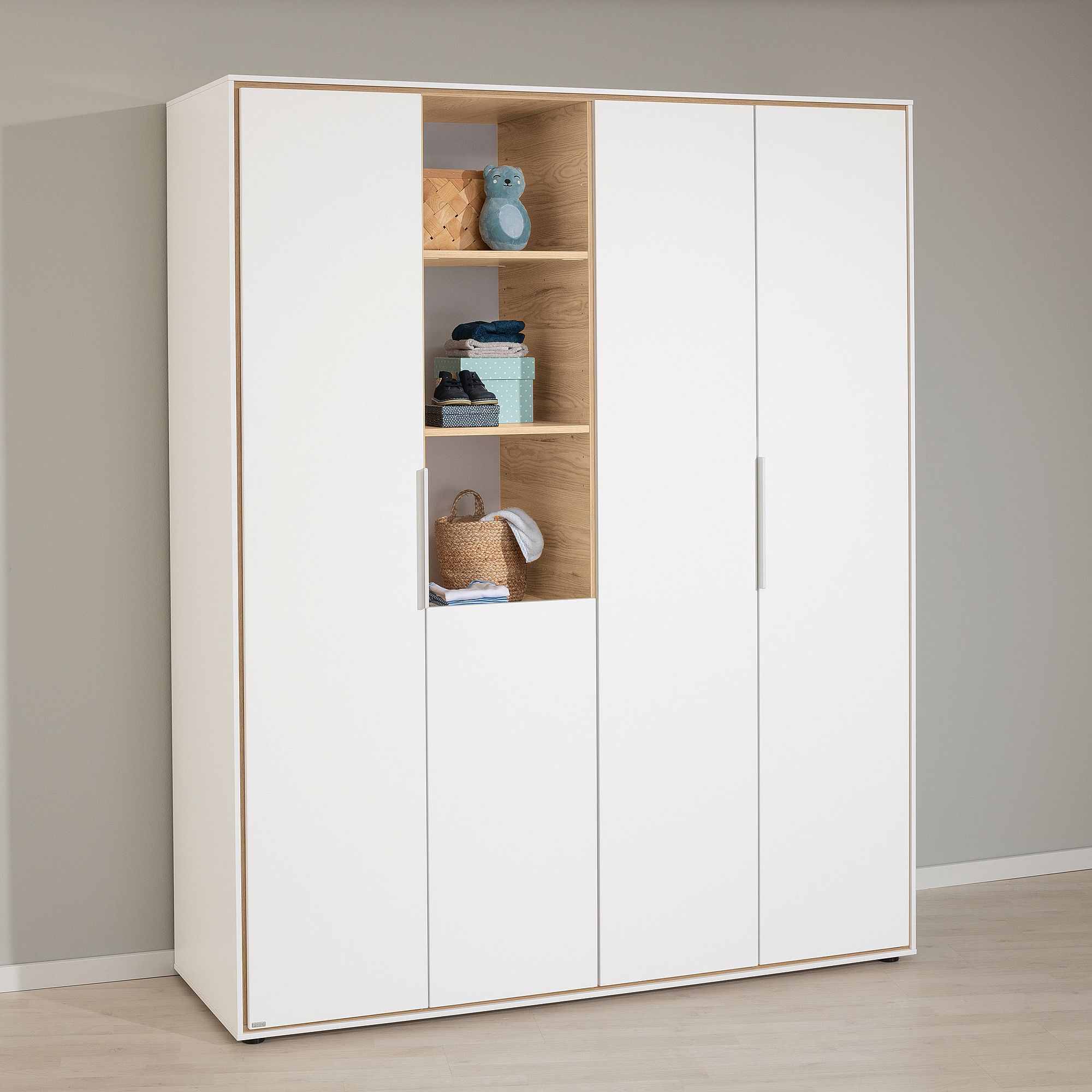 Weißer Kleiderschrank mit Holzregalen, in denen Spielzeug, Körbe und gefaltete Kleidung aufbewahrt werden.