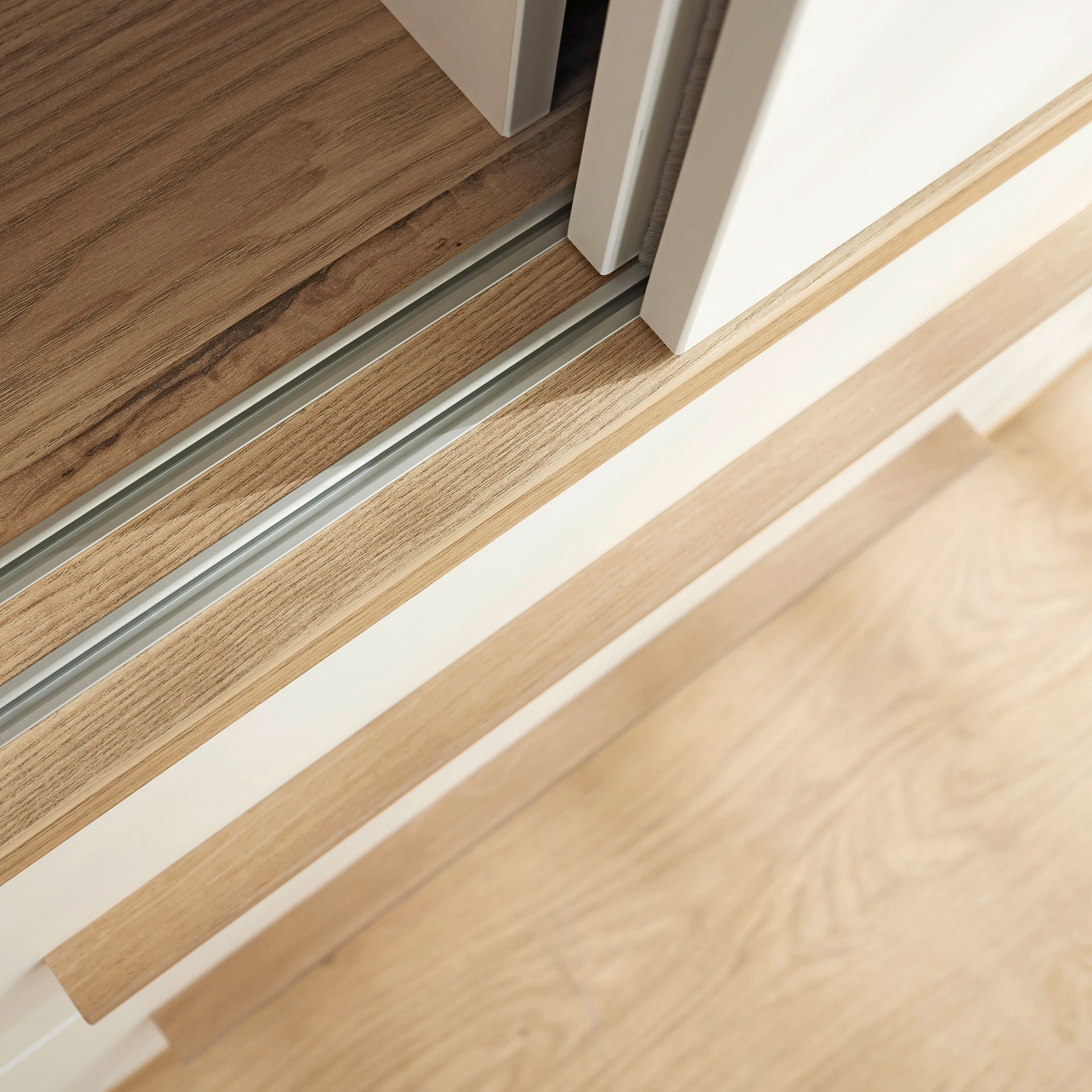 Schiebetürenschrank Yolanda mit 2 Schiebetüren und 2 Schubladen in 164 cm Nahaufnahme einer hölzernen Schiebetürschiene auf einem hellen Holzboden.