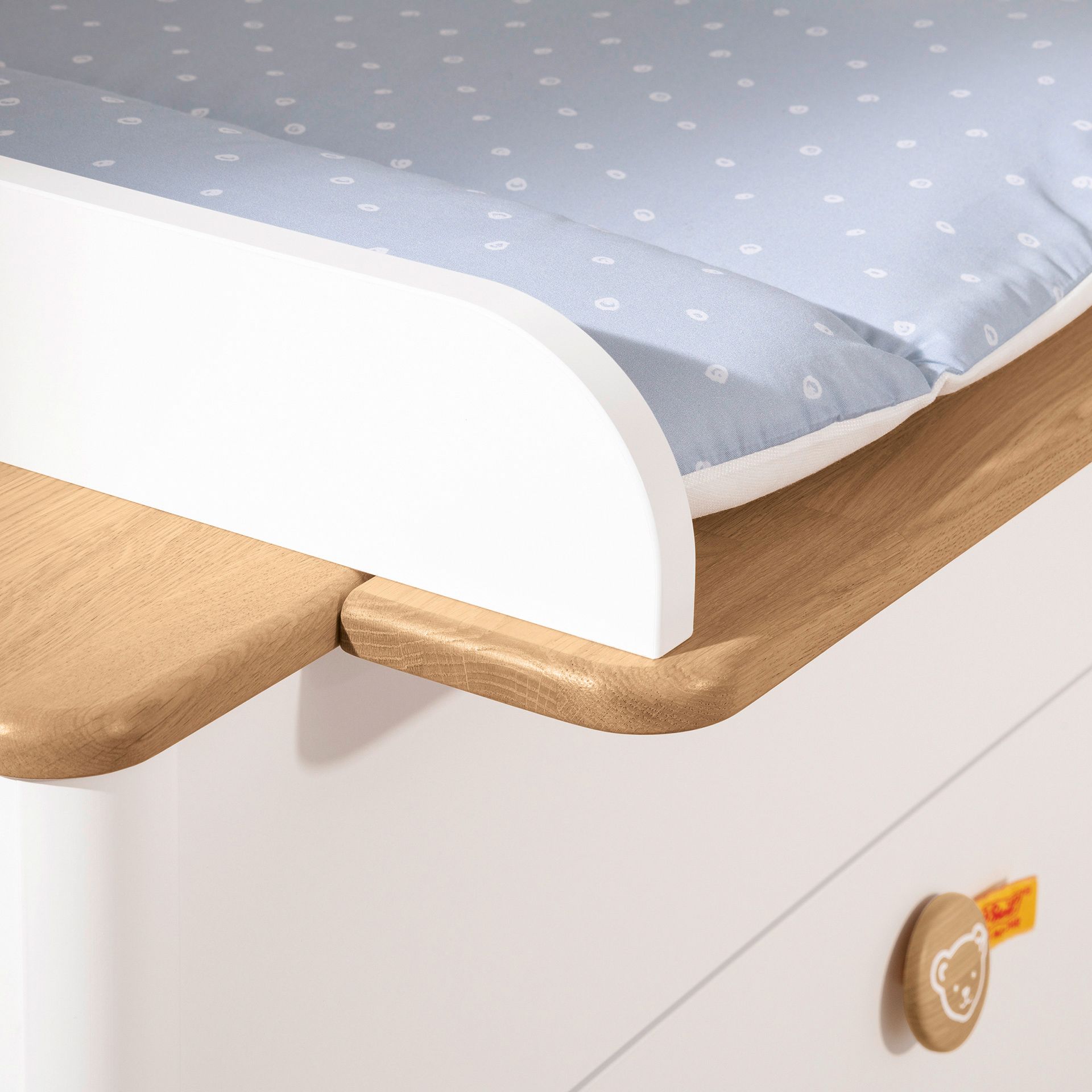 Wickelaufsatz Lotte & Fynn - Steiff by PAIDI zur Erweiterung der Wickelkommode mit 3 Schubladen Nahaufnahme eines hölzernen Wickeltisches mit einer blau gemusterten Wickelauflage.