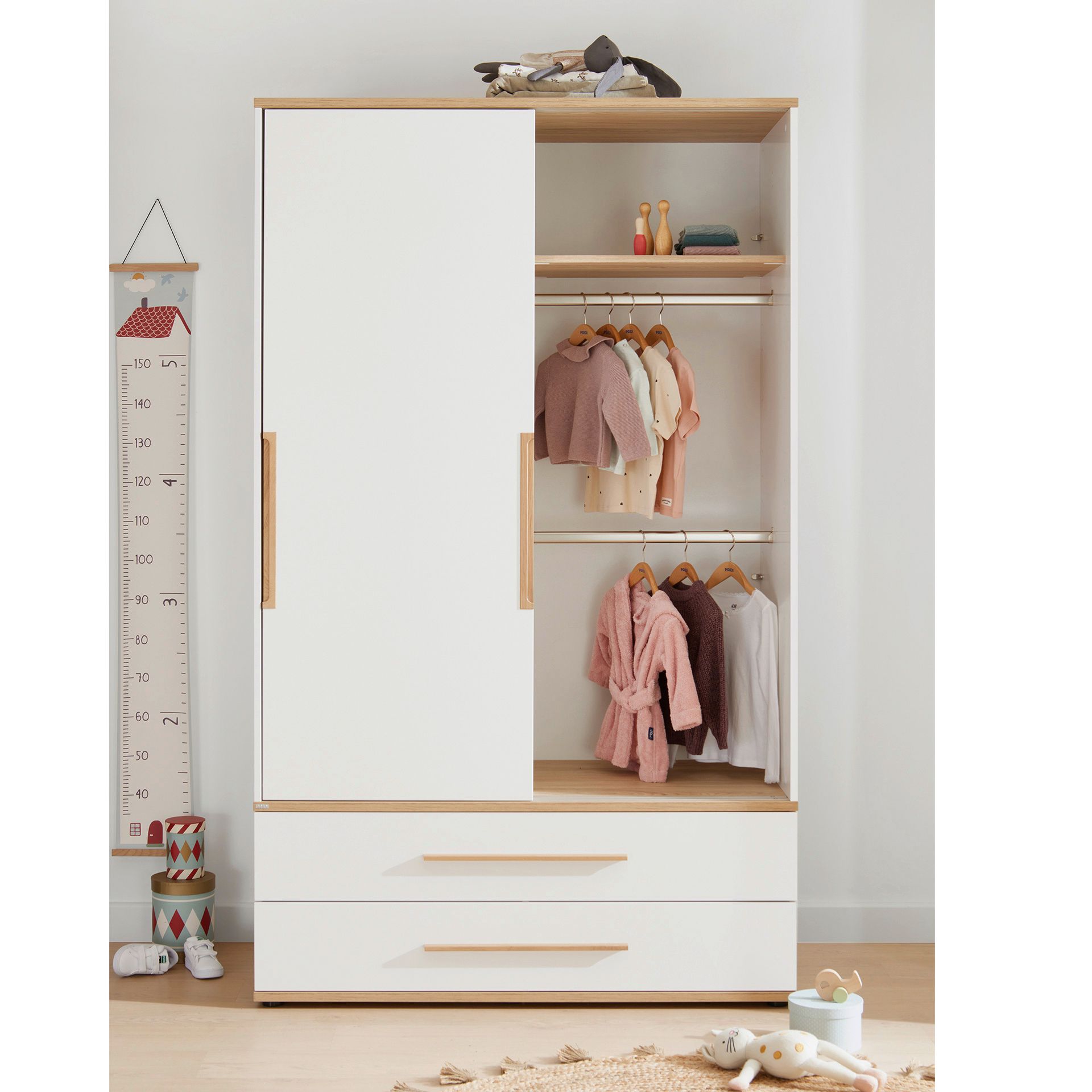 Schiebetürenschrank Yolanda mit 2 Schiebetüren und 2 Schubladen in 123,5 cm Weißer Kleiderschrank mit Schiebetüren, Kinderkleidung und Spielzeug in einem aufgeräumten Zimmer.