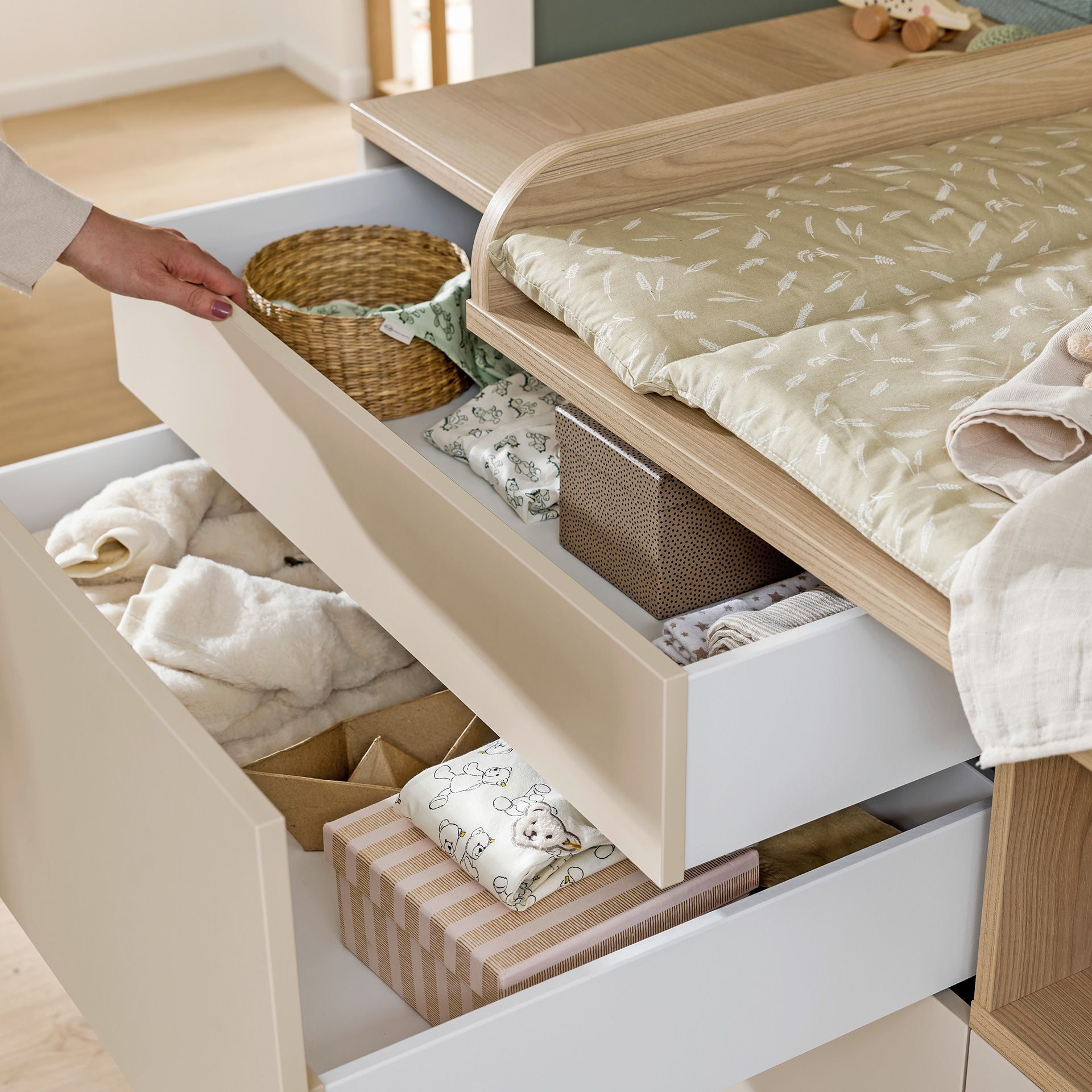 Eine Person öffnet eine Kommodenschublade, die mit fein säuberlich geordneter Babykleidung und Schachteln gefüllt ist.