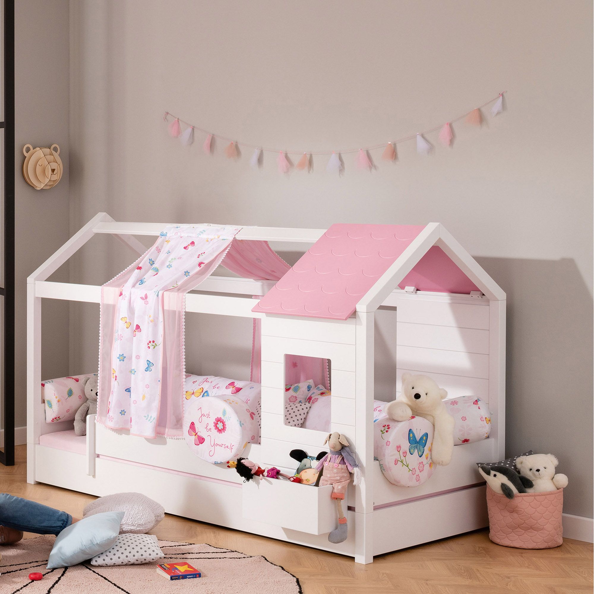 Weißes, hausförmiges Bett mit rosa Akzenten, Plüschtieren und pastellfarbenem Dekor.