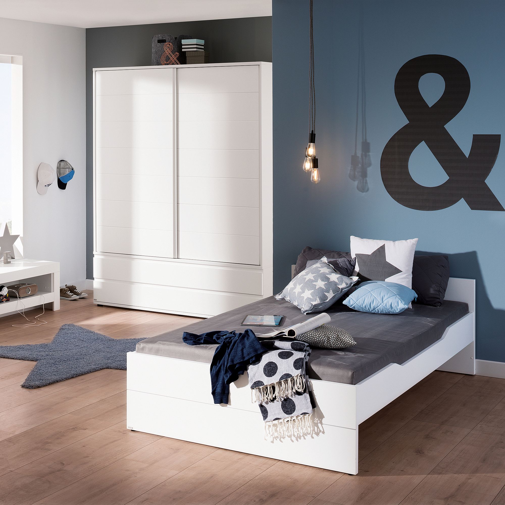 Modernes Schlafzimmer mit einem weißen Bett, blauen Wänden und hängenden Glühbirnen.
