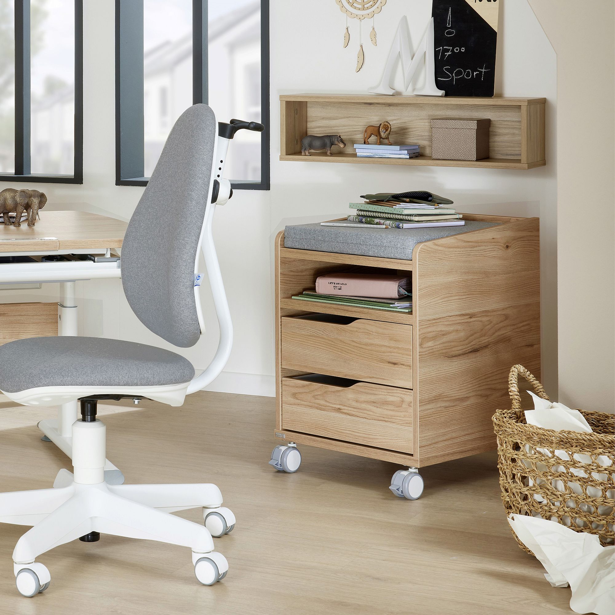 Modern home office with a wooden desk, gray chair, and storage unit on wheels.