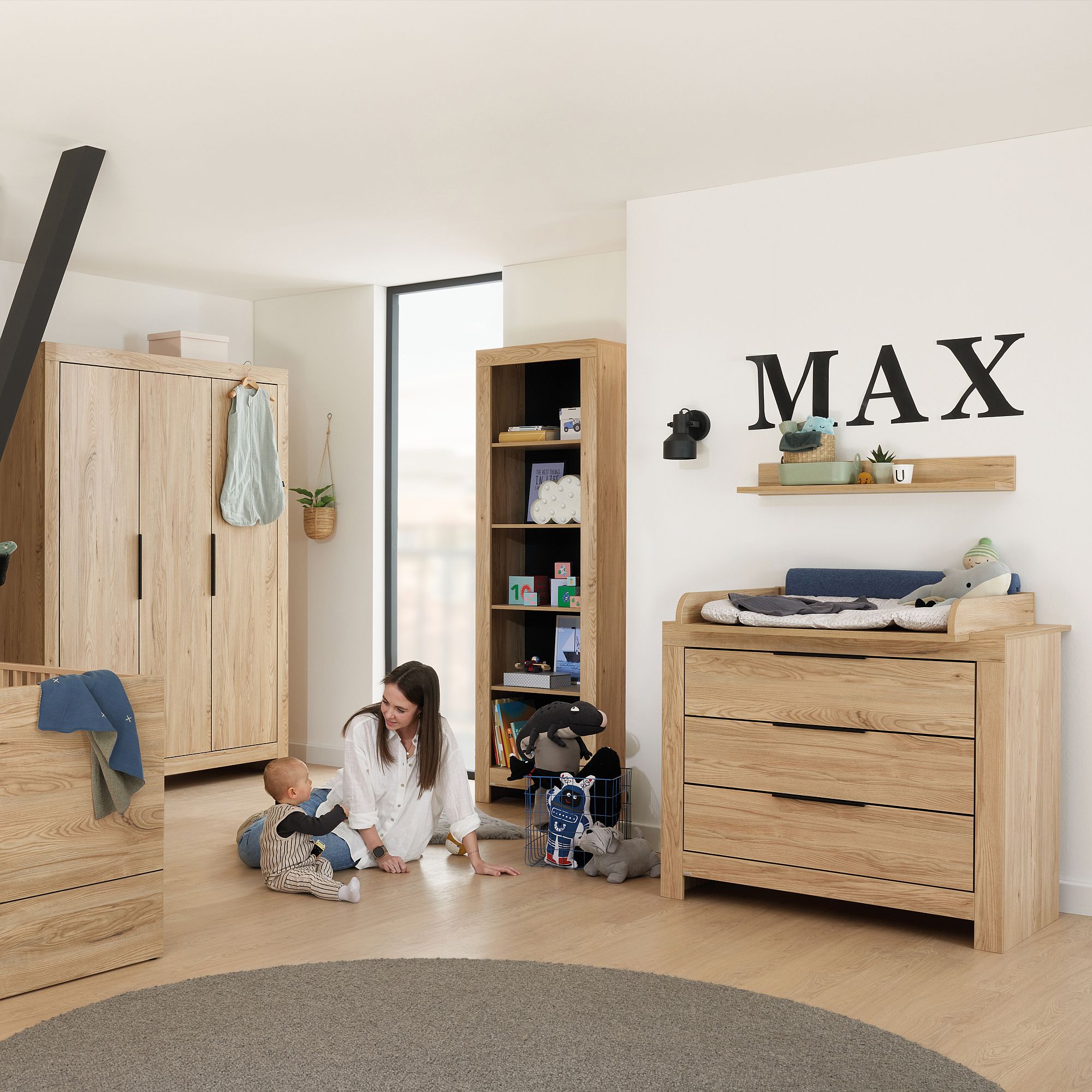Eine Frau und ein Baby spielen in einem Kinderzimmer mit Holzmöbeln und MAX an der Wand.