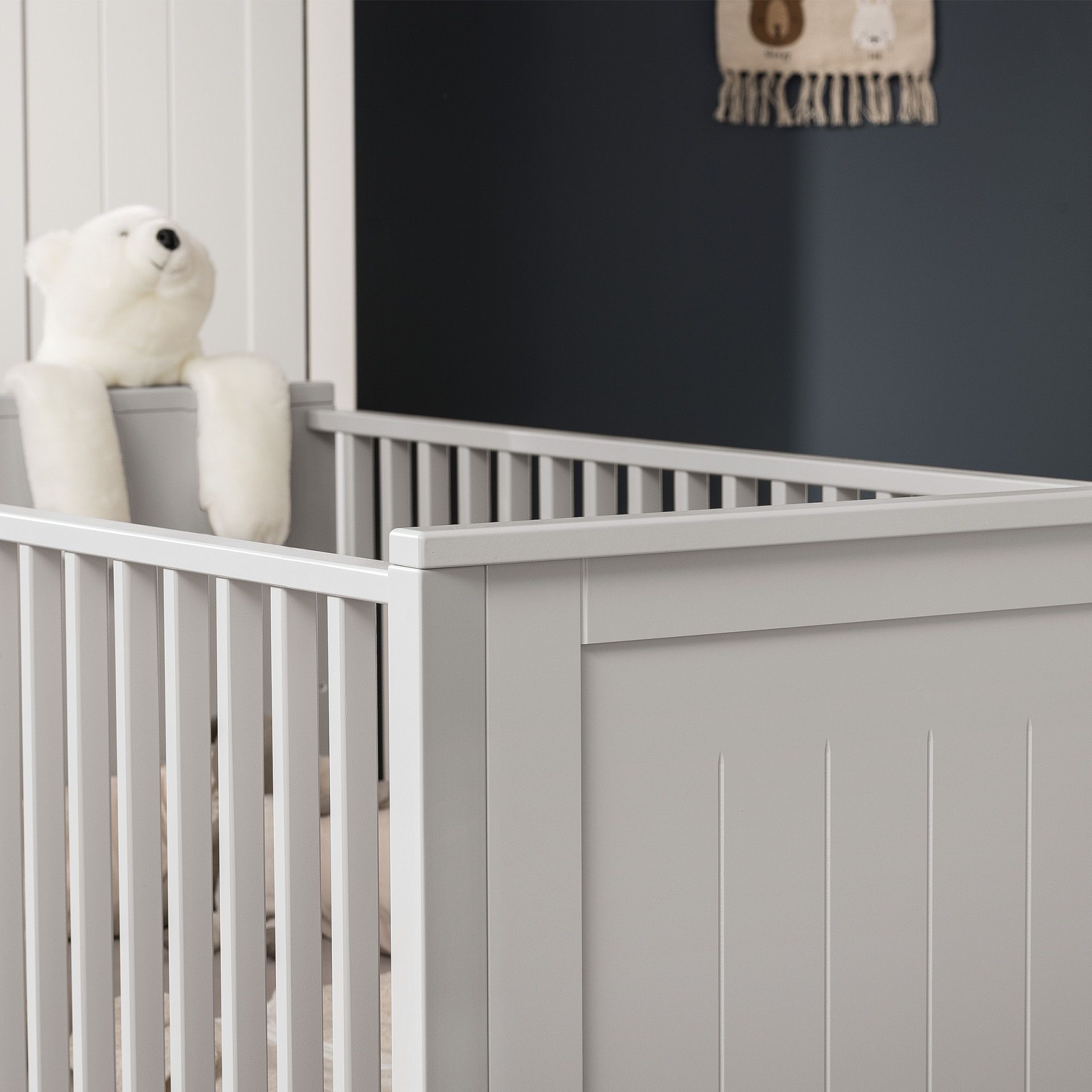 White crib with a white teddy bear draped over the side in a nursery room.