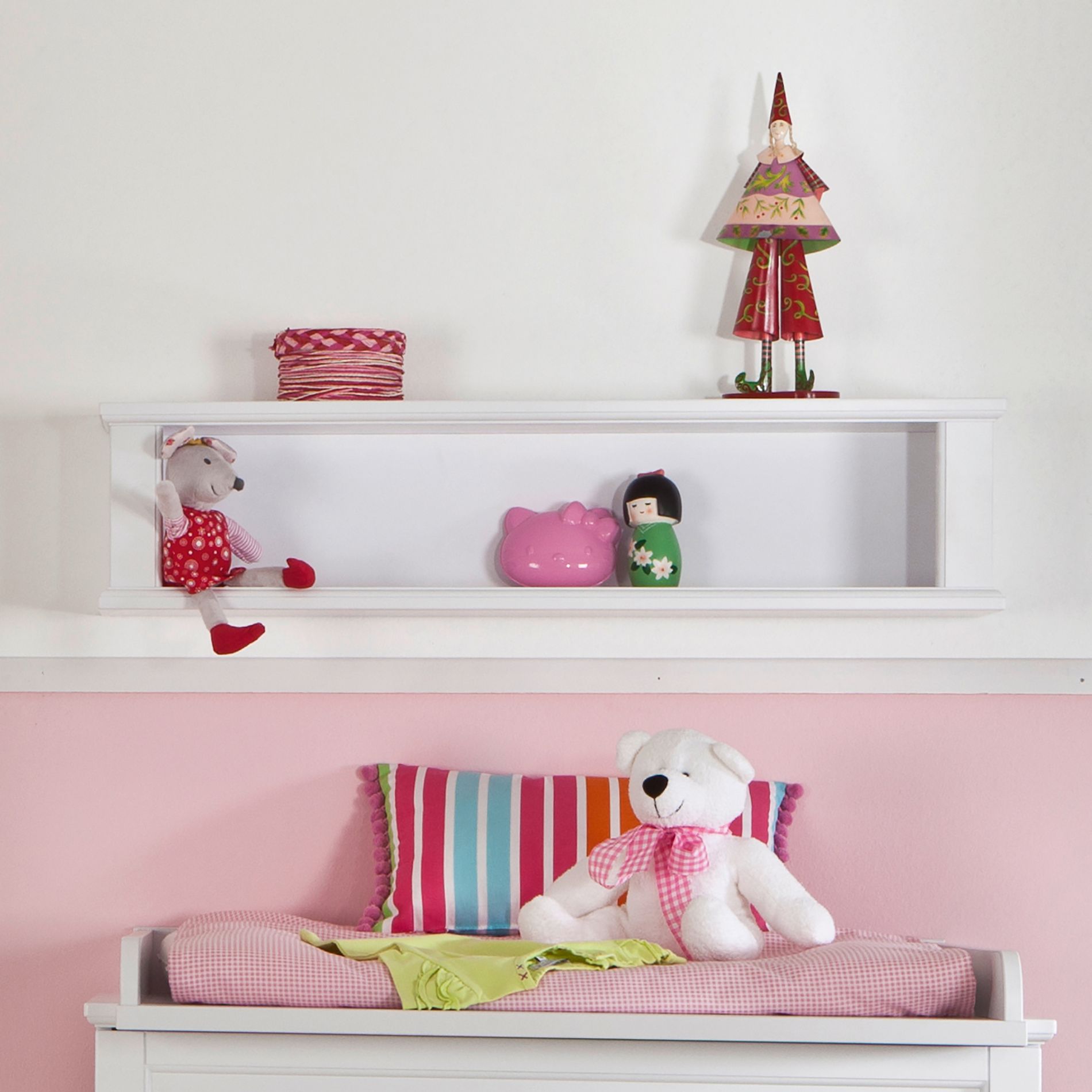 White shelf with toys above a changing table with a teddy bear and striped pillow.