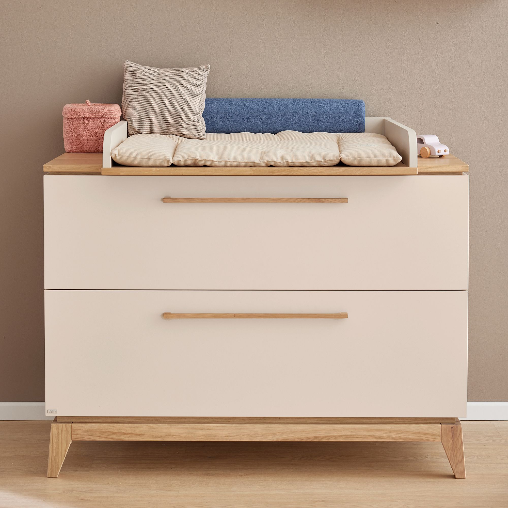 Moderne Kommode mit Wickelauflage und Babyutensilien auf der Oberseite vor einer beigen Wand.