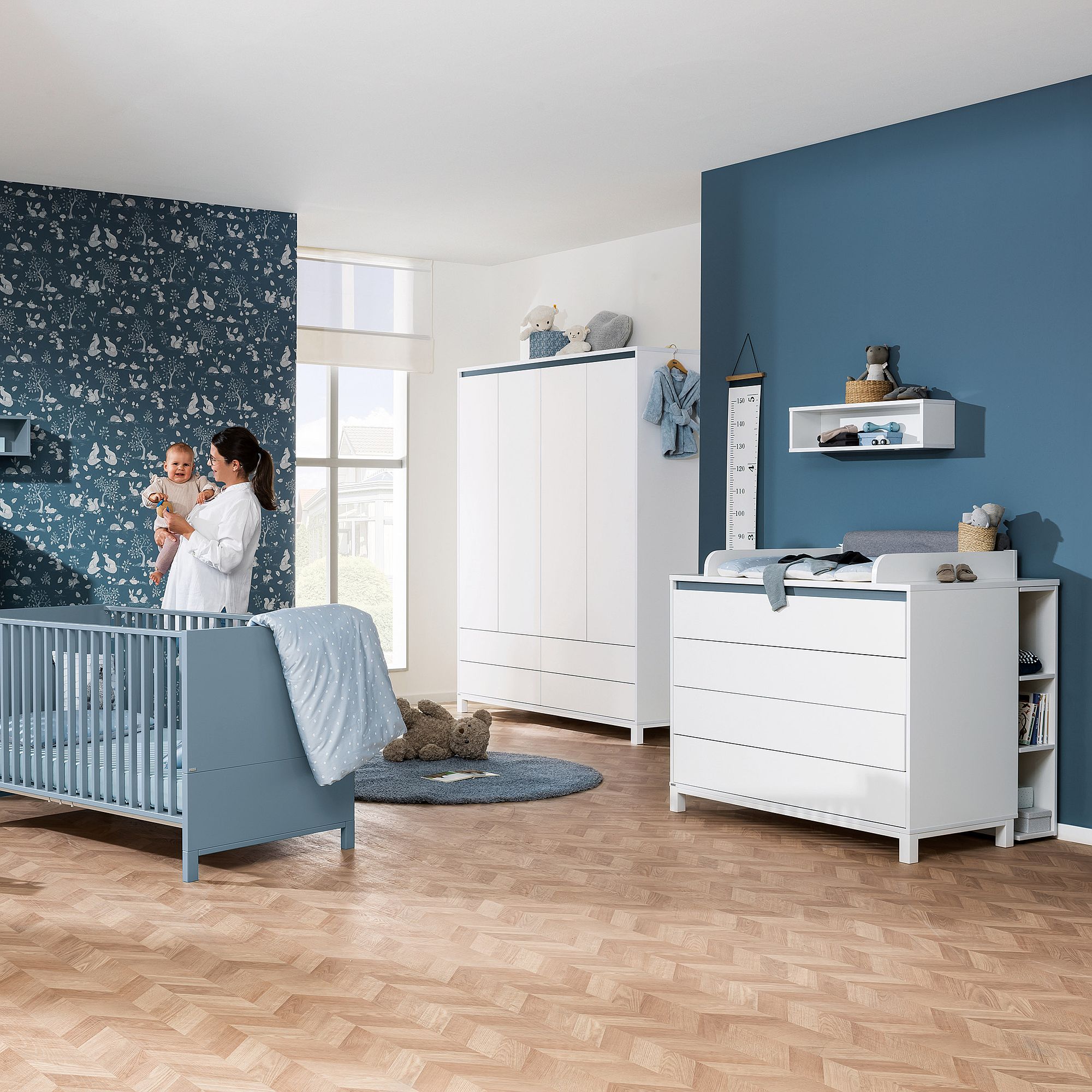 Ein modernes blau-weißes Kinderzimmer mit einem Kinderbett, einem Kleiderschrank und einem Wickeltisch.
