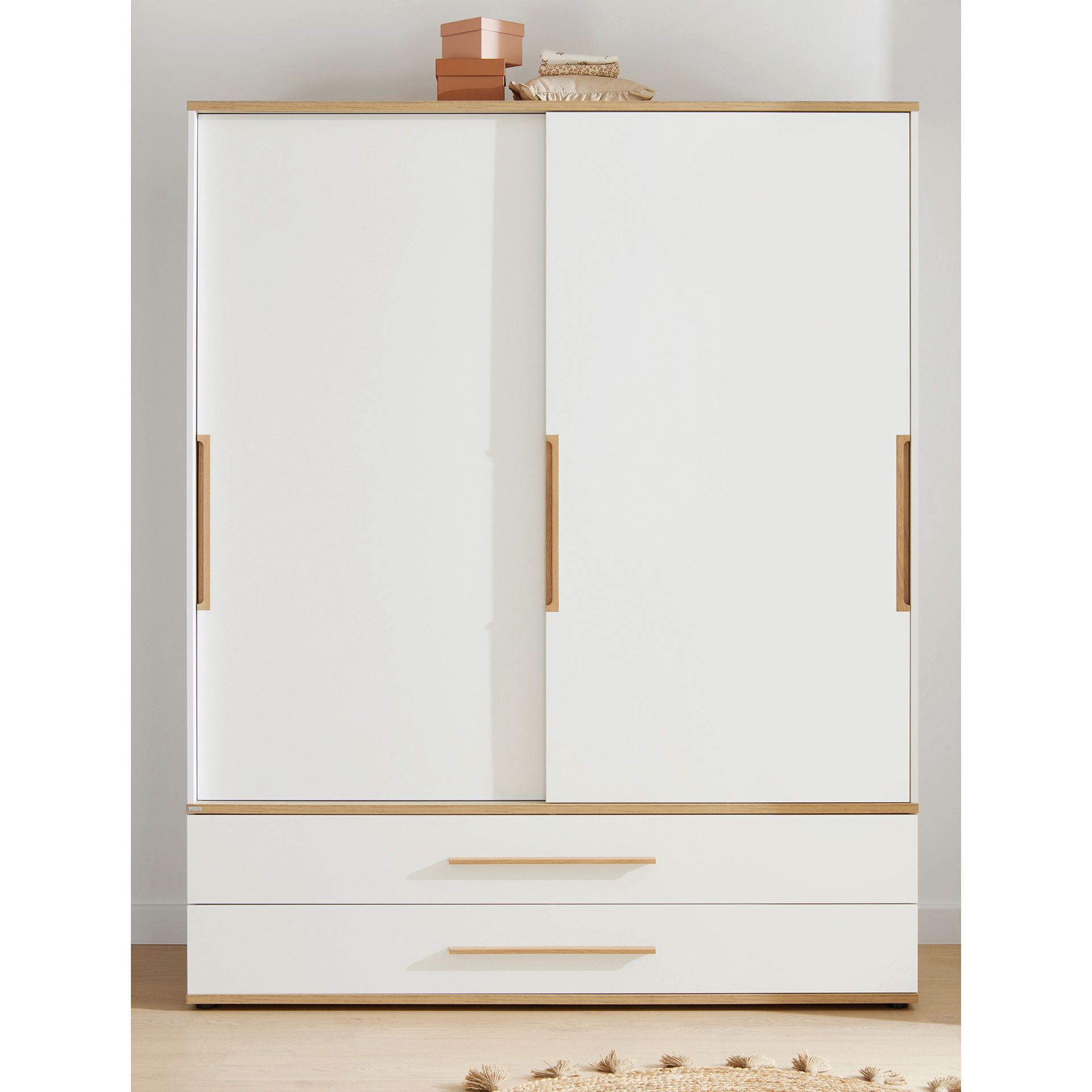 Weißer Kleiderschrank mit Schiebetüren, zwei Schubladen und Dekorationselementen auf der Oberseite.