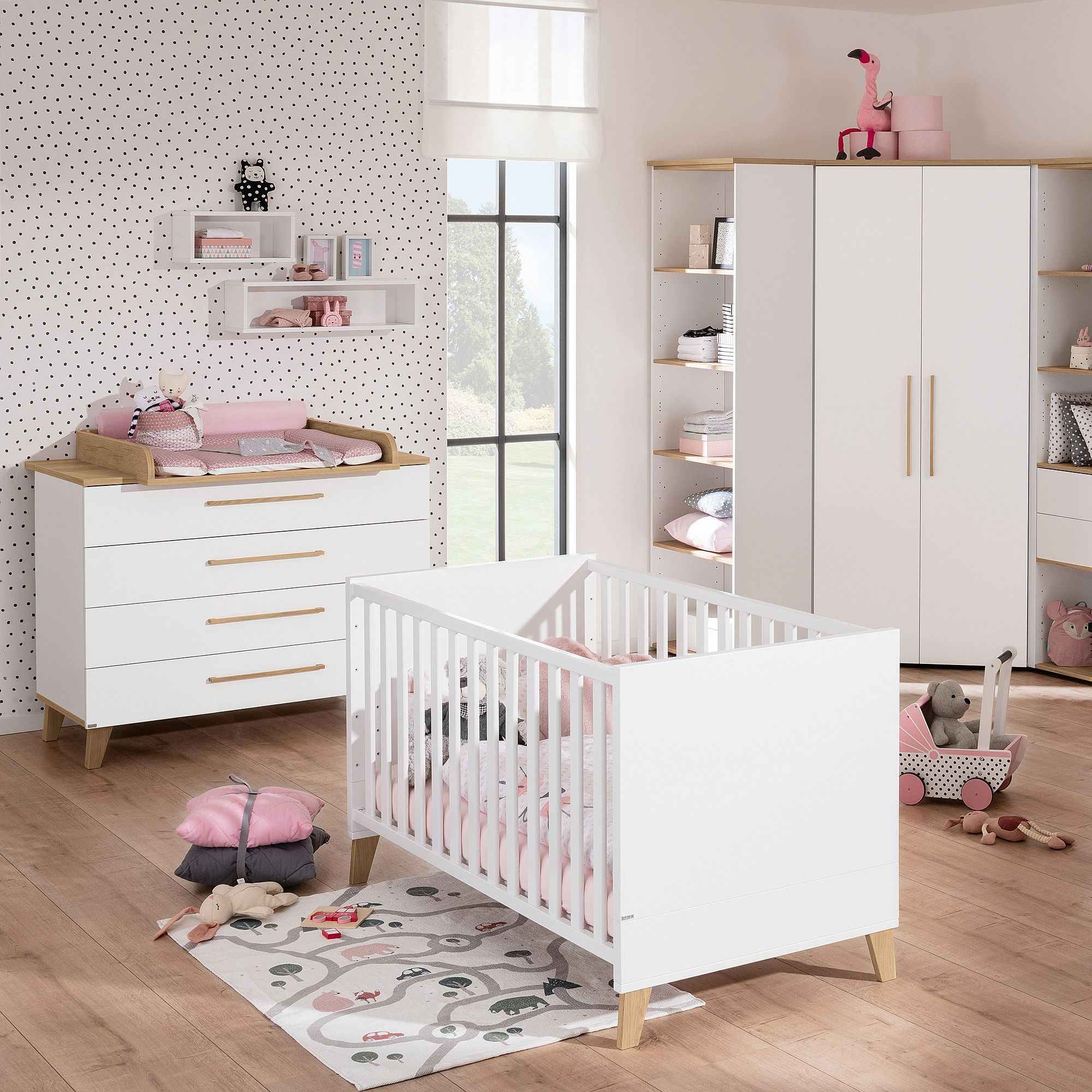 Ein modernes Kinderzimmer mit weißen Möbeln, zartrosa Akzenten und Spielzeug auf dem Boden.