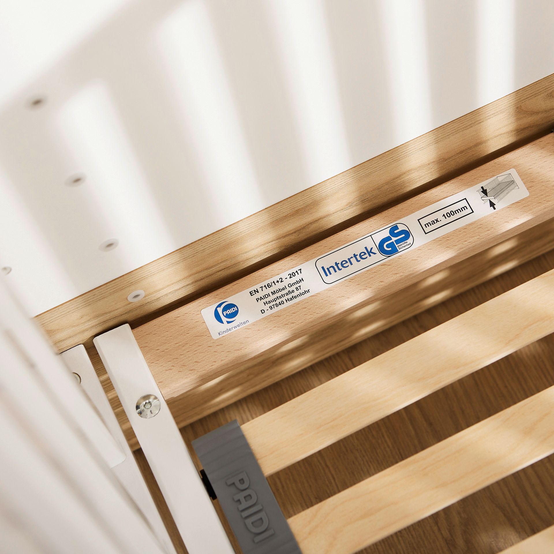 Close-up of a wooden crib frame with certification and safety labels attached.