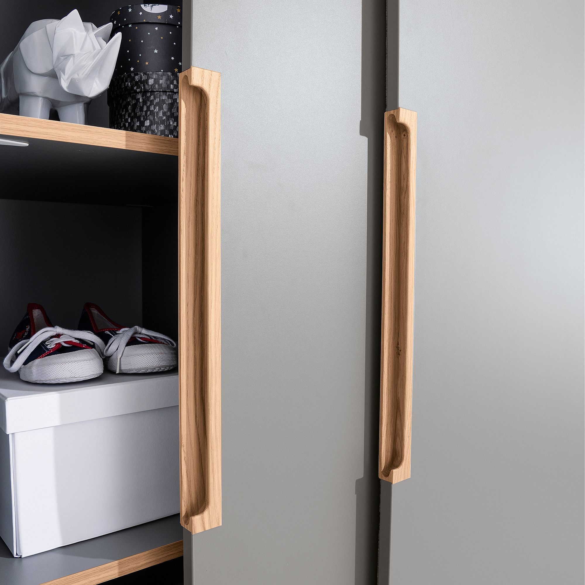 Nahaufnahme von Holzgriffen an einem Schrank, in dem sich Regale mit Schuhen und einer Taschentuchschachtel befinden.