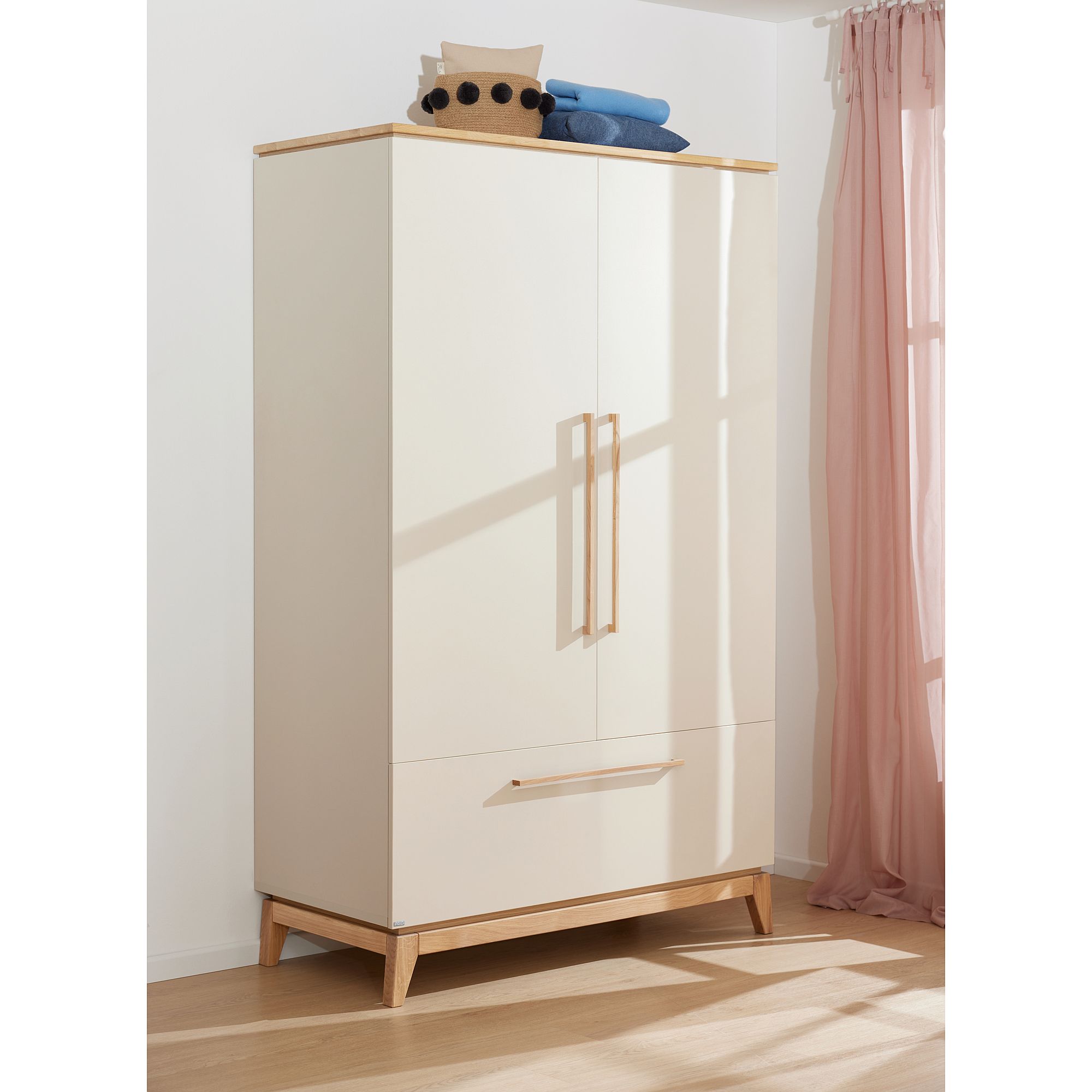 Beiger Kleiderschrank mit Holzgriffen, einem Korb und gefalteten Handtüchern darauf.
