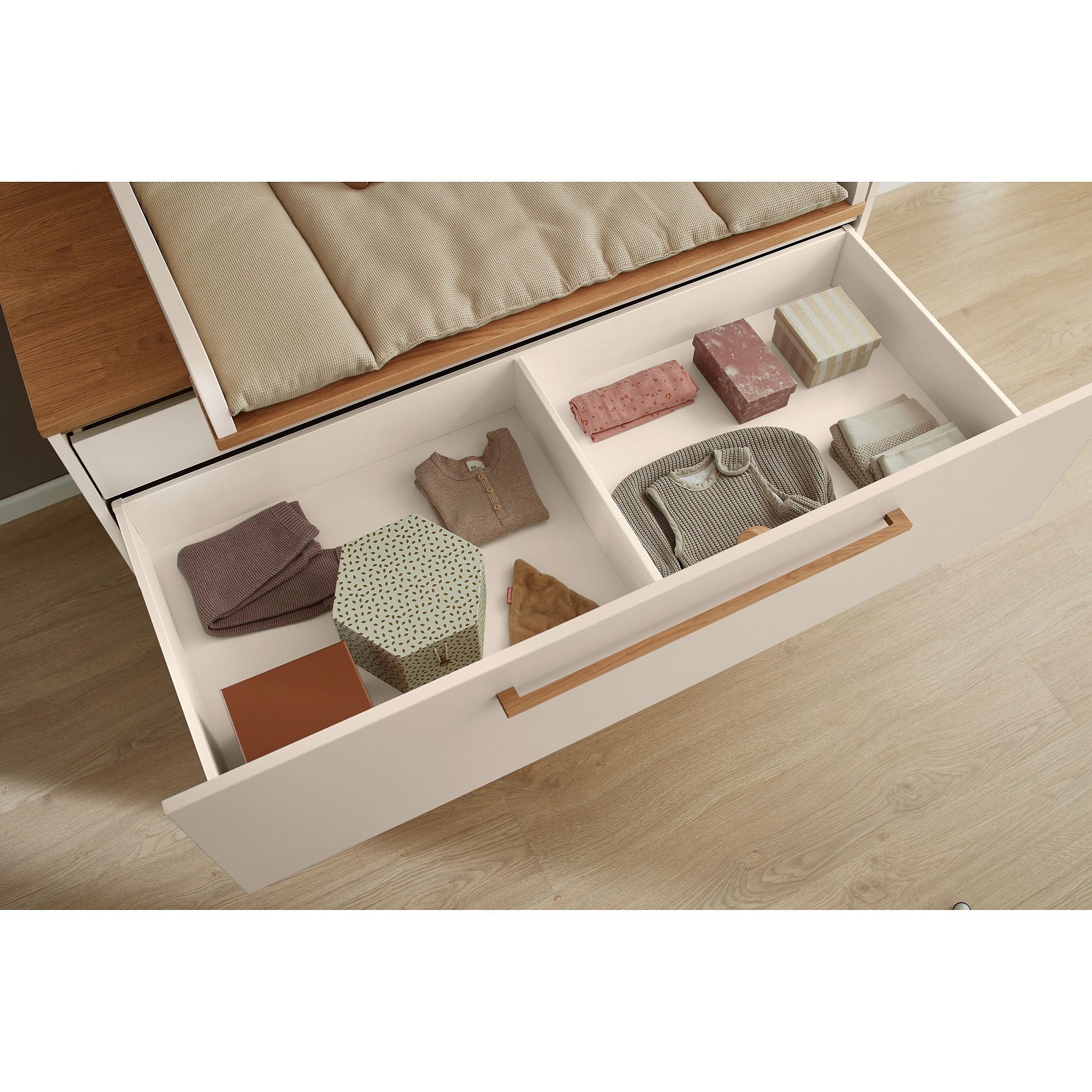 Offene Schublade mit ordentlich gefalteter Kleidung und gemusterten Kisten auf einem Holzboden.