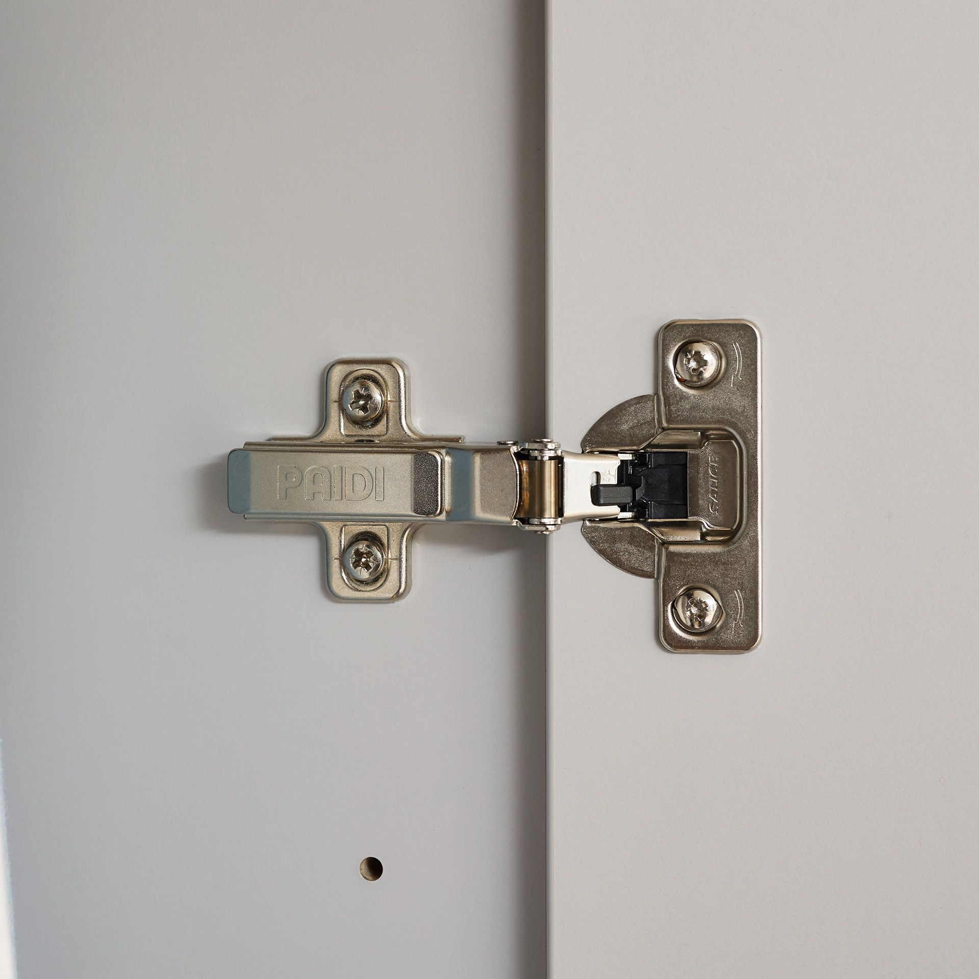 Drehtürenschrank Fiene mit 3 Türen und 1 Schublade Nahaufnahme eines Metallscharniers, das an einer weißen Schranktür befestigt ist.