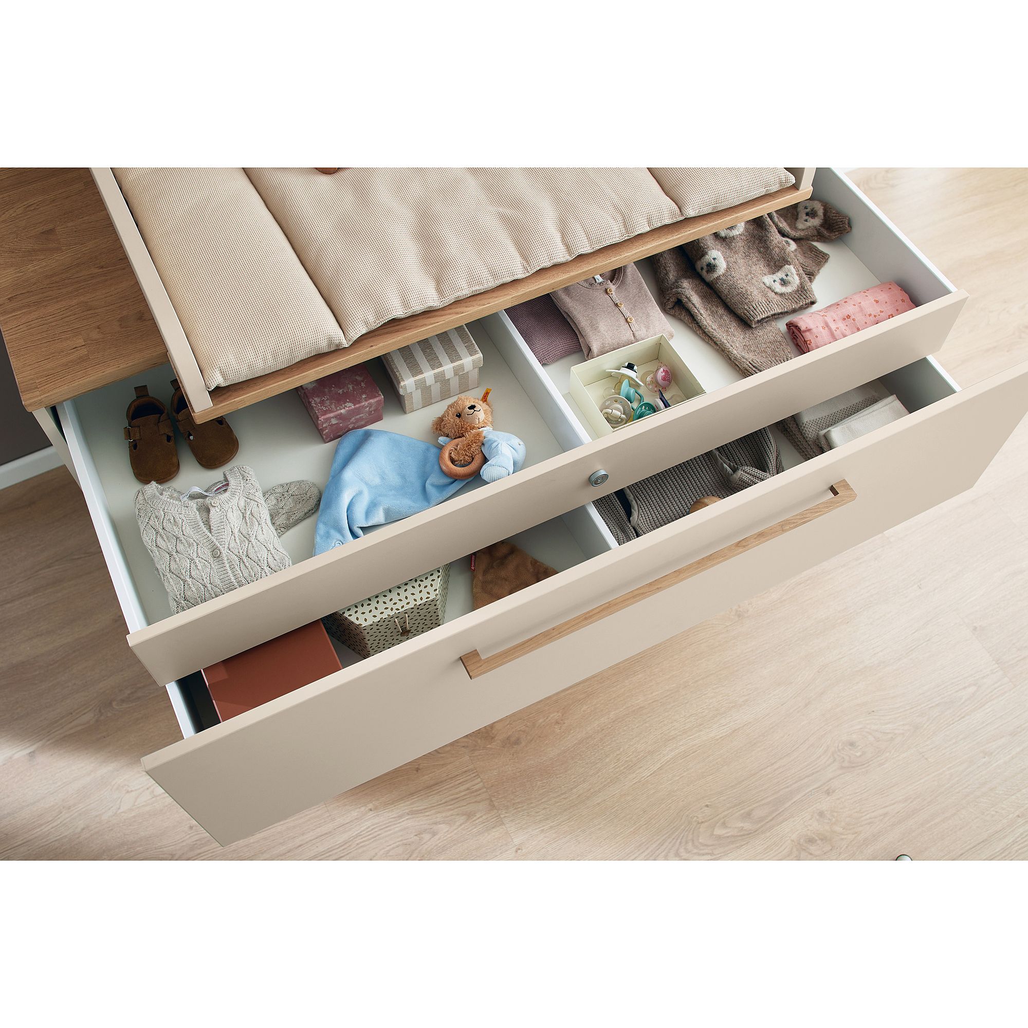 Offene Schublade mit ordentlich organisierter Babykleidung, Spielzeug und Decken darin.