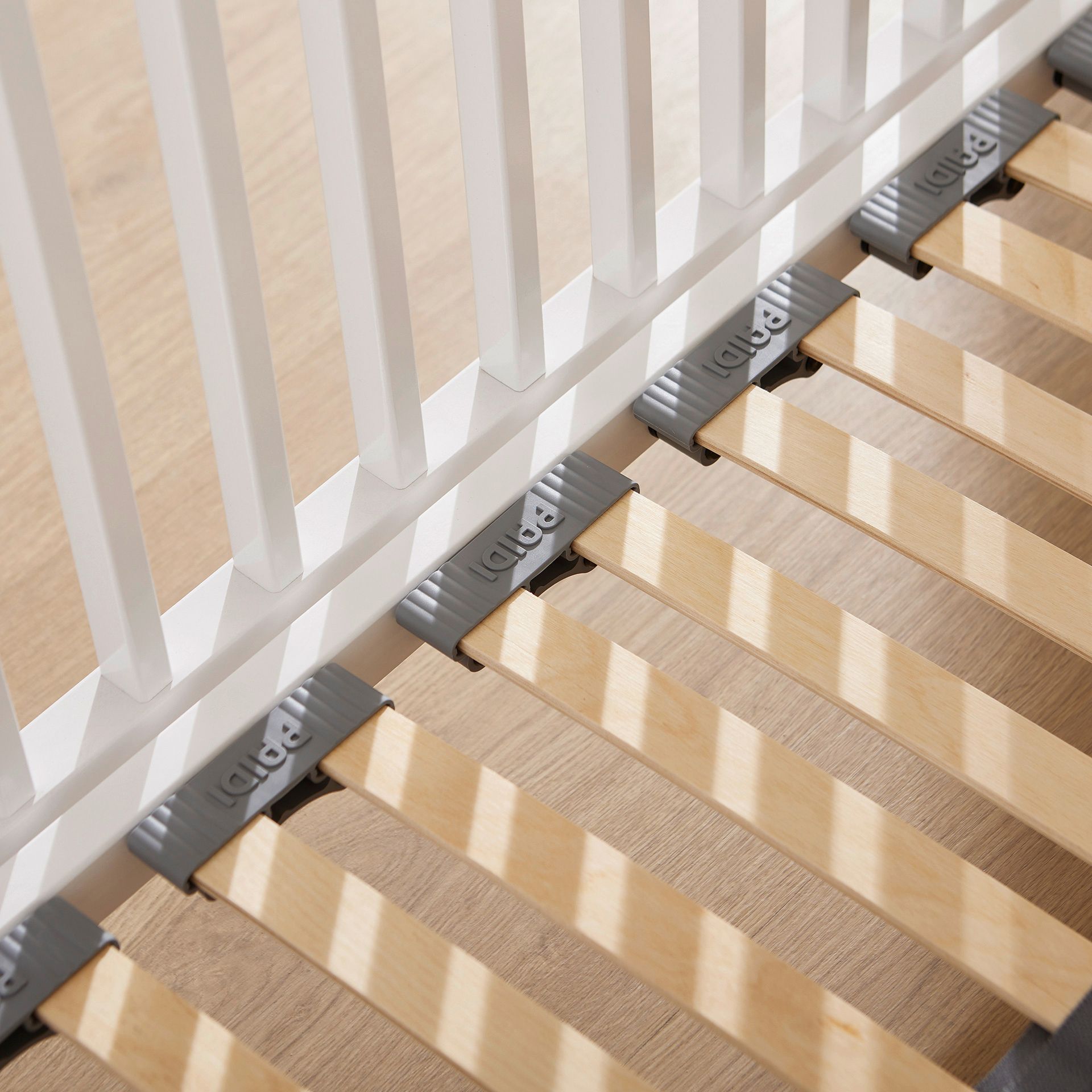 Wooden crib slats and support bars with white rails on a light wooden floor.