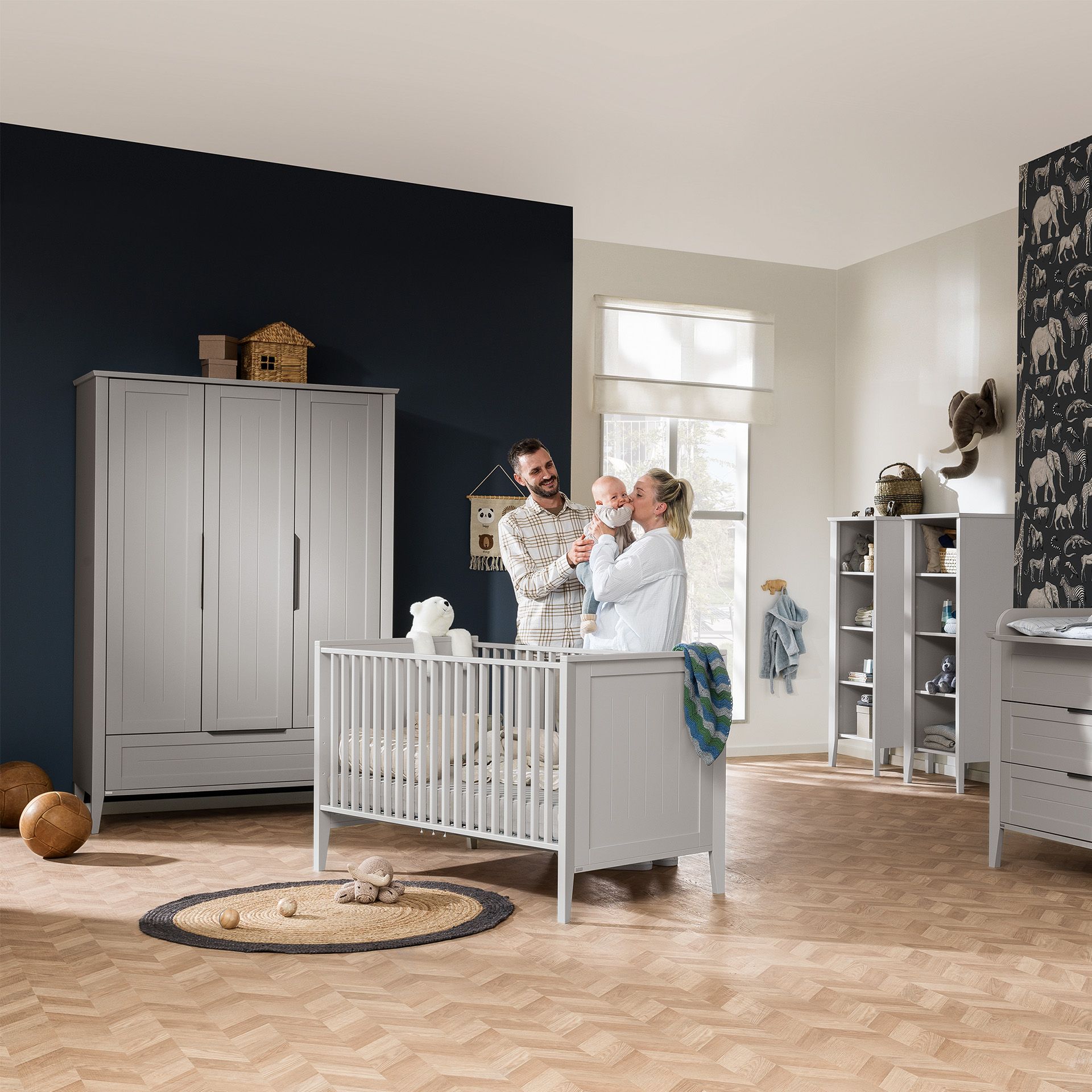 Babybett Levke 70 x 140 cm Ein Paar steht an einem Kinderbett mit einem Baby in einem modernen Kinderzimmer.
