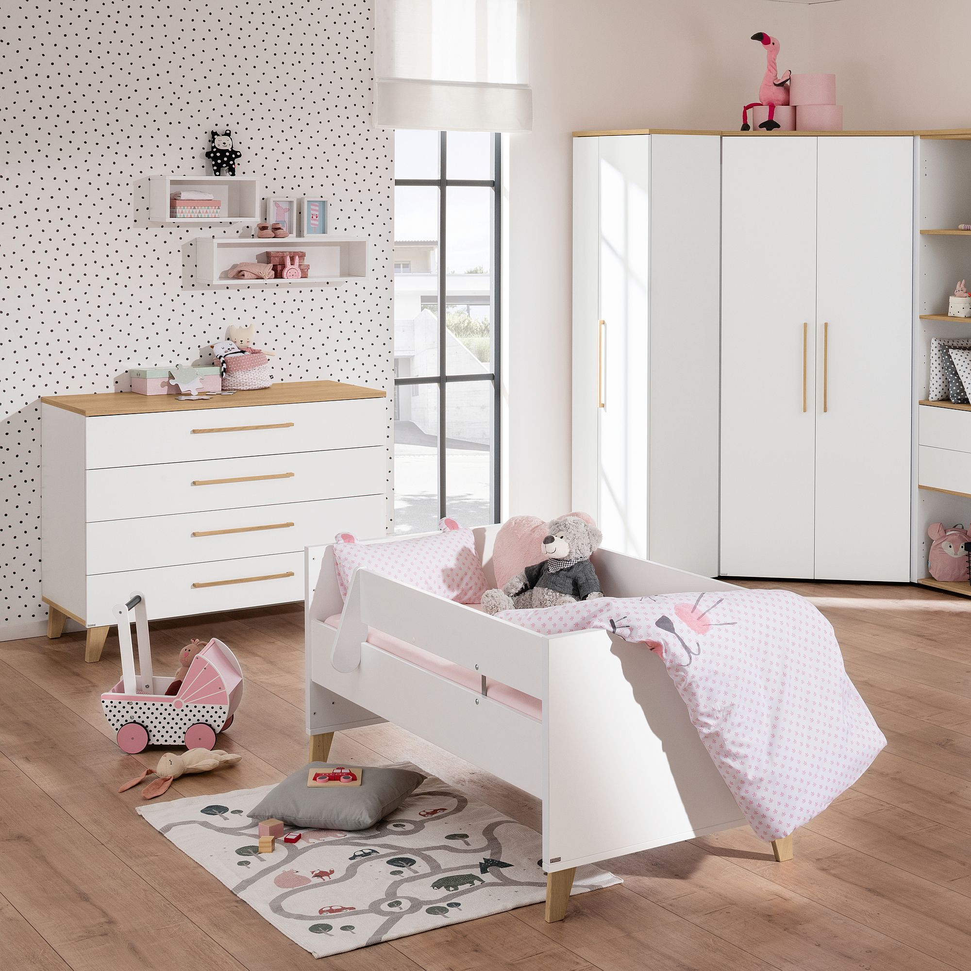 Modernes Kinderzimmer mit weißen Möbeln, rosa Akzenten und Plüschtieren auf dem Bett.