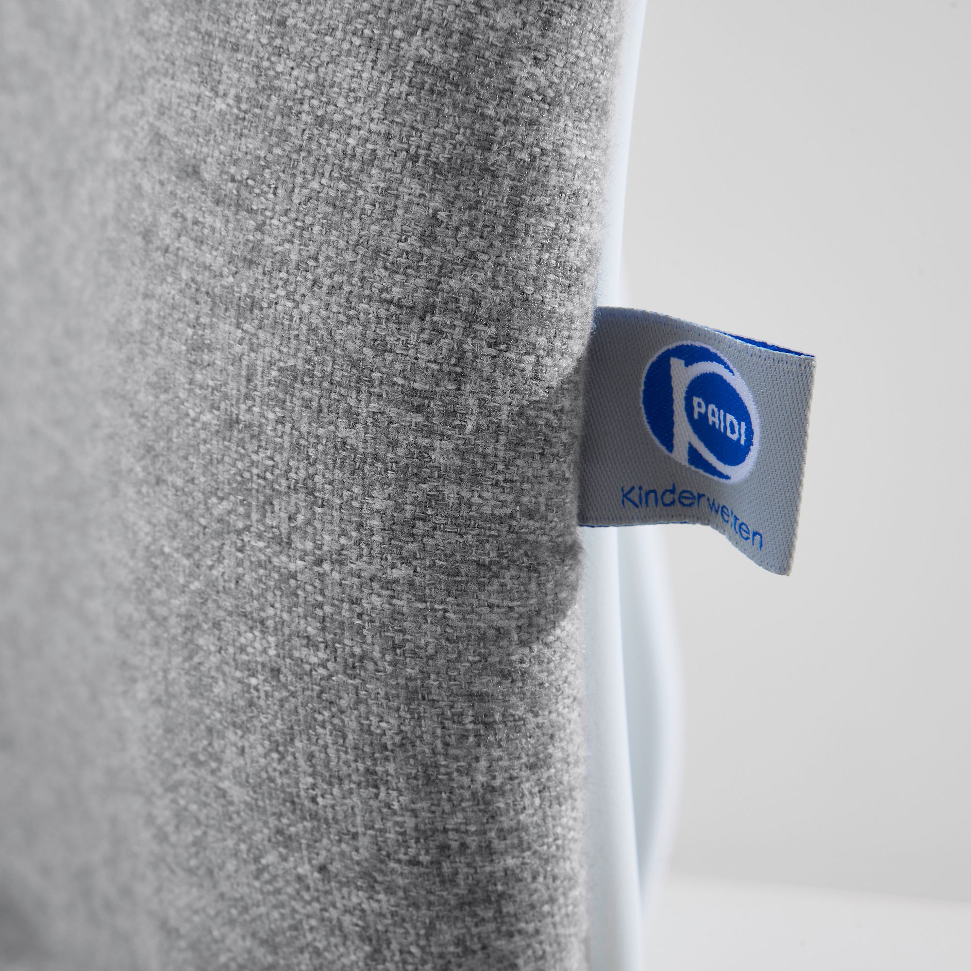 Close-up of a gray fabric with a blue and white Kinderkraft tag attached.