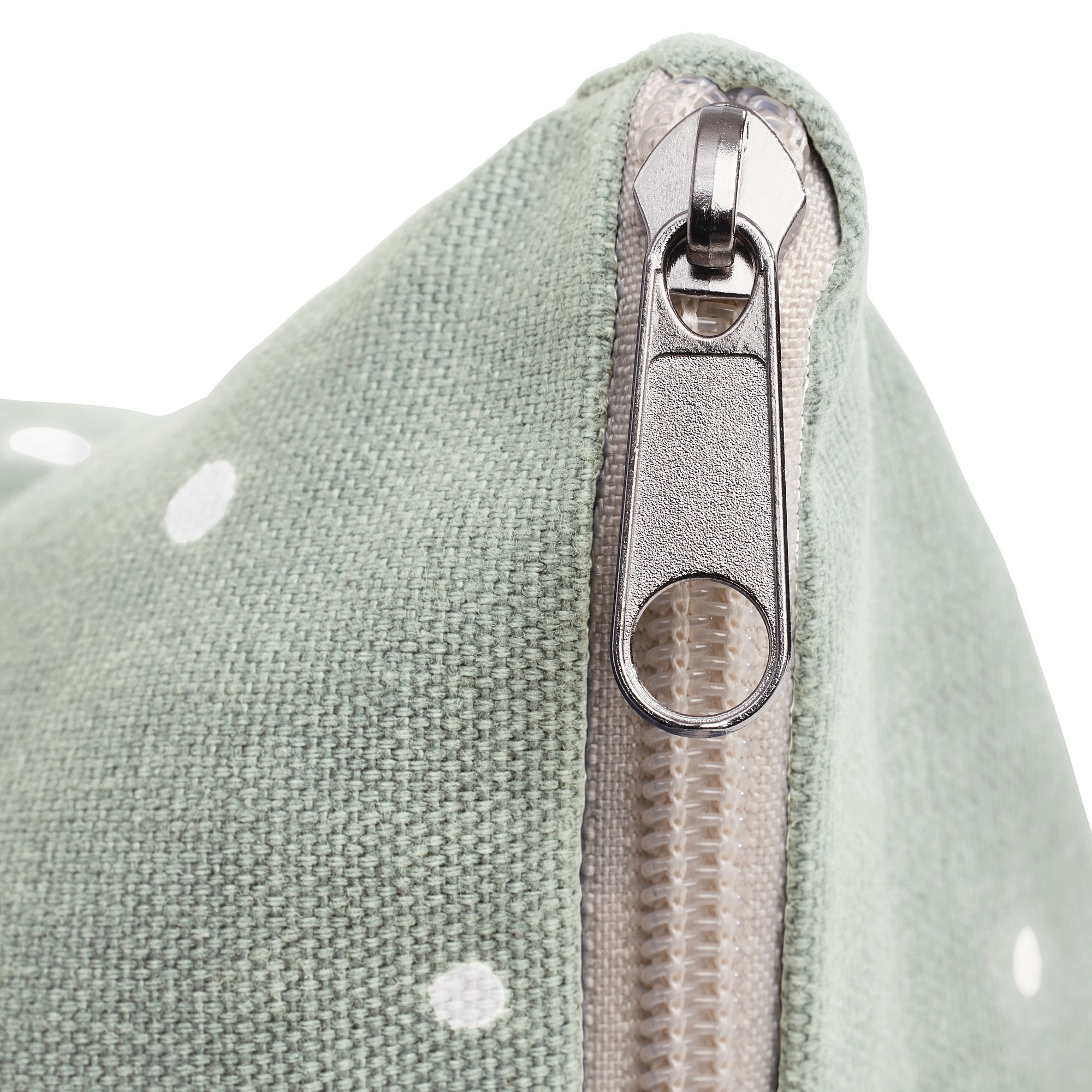 Nahaufnahme eines silbernen Reißverschlusses an einer grünen Stofftasche mit weißen Tupfen.