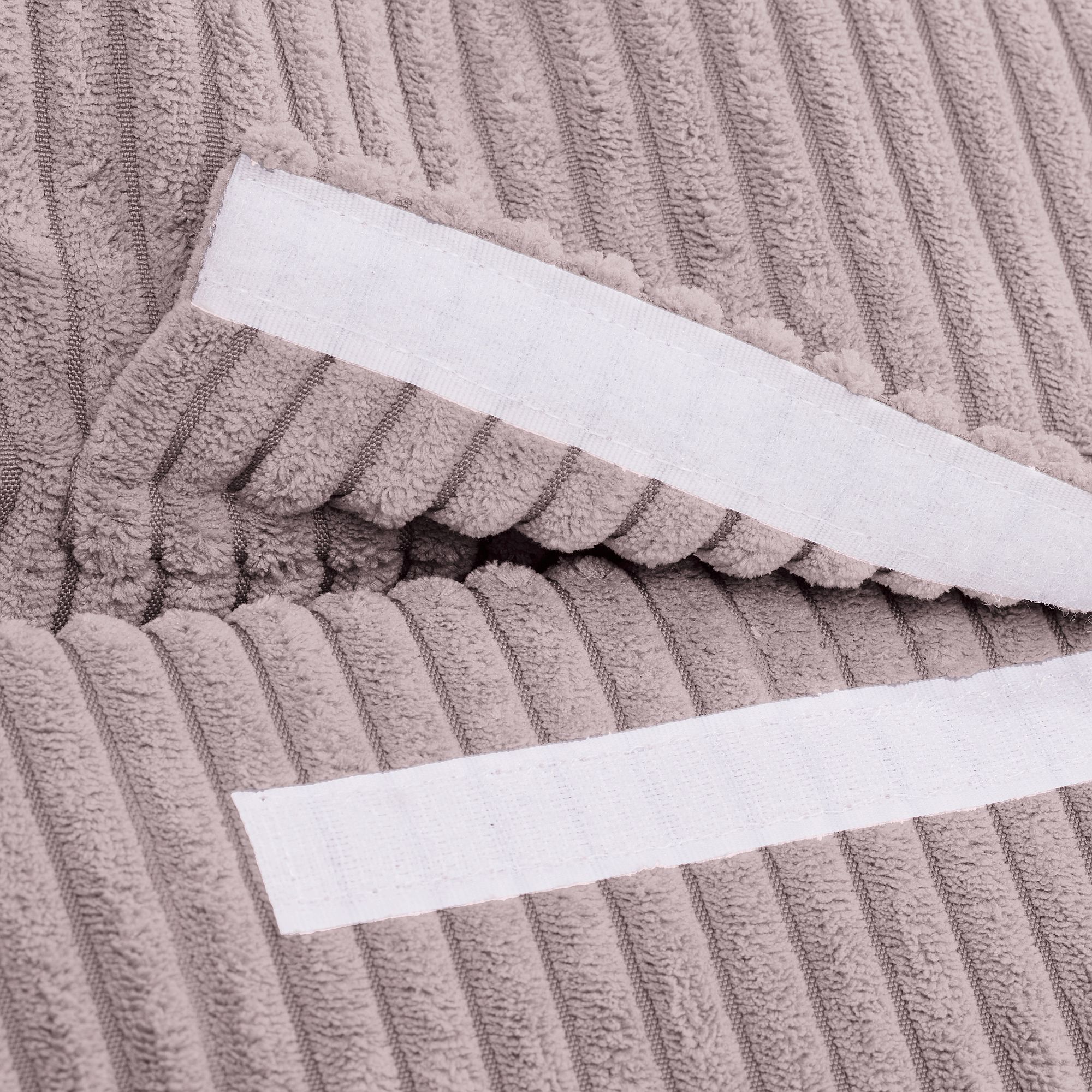 Nahaufnahme eines strukturierten beigen Stoffes, an dem zwei weiße Streifen befestigt sind.