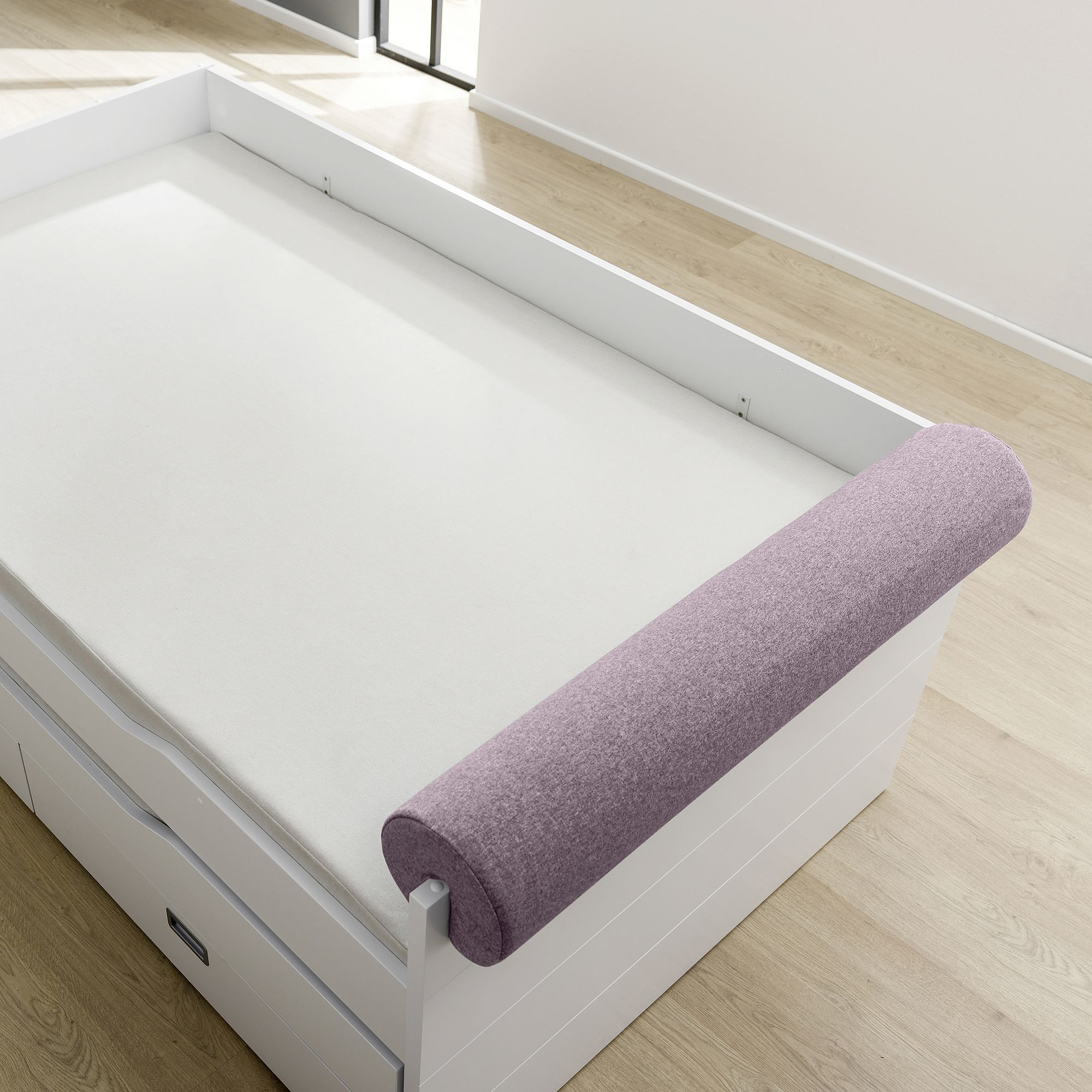 White bed with a light purple cylindrical cushion on the edge in a bright room.