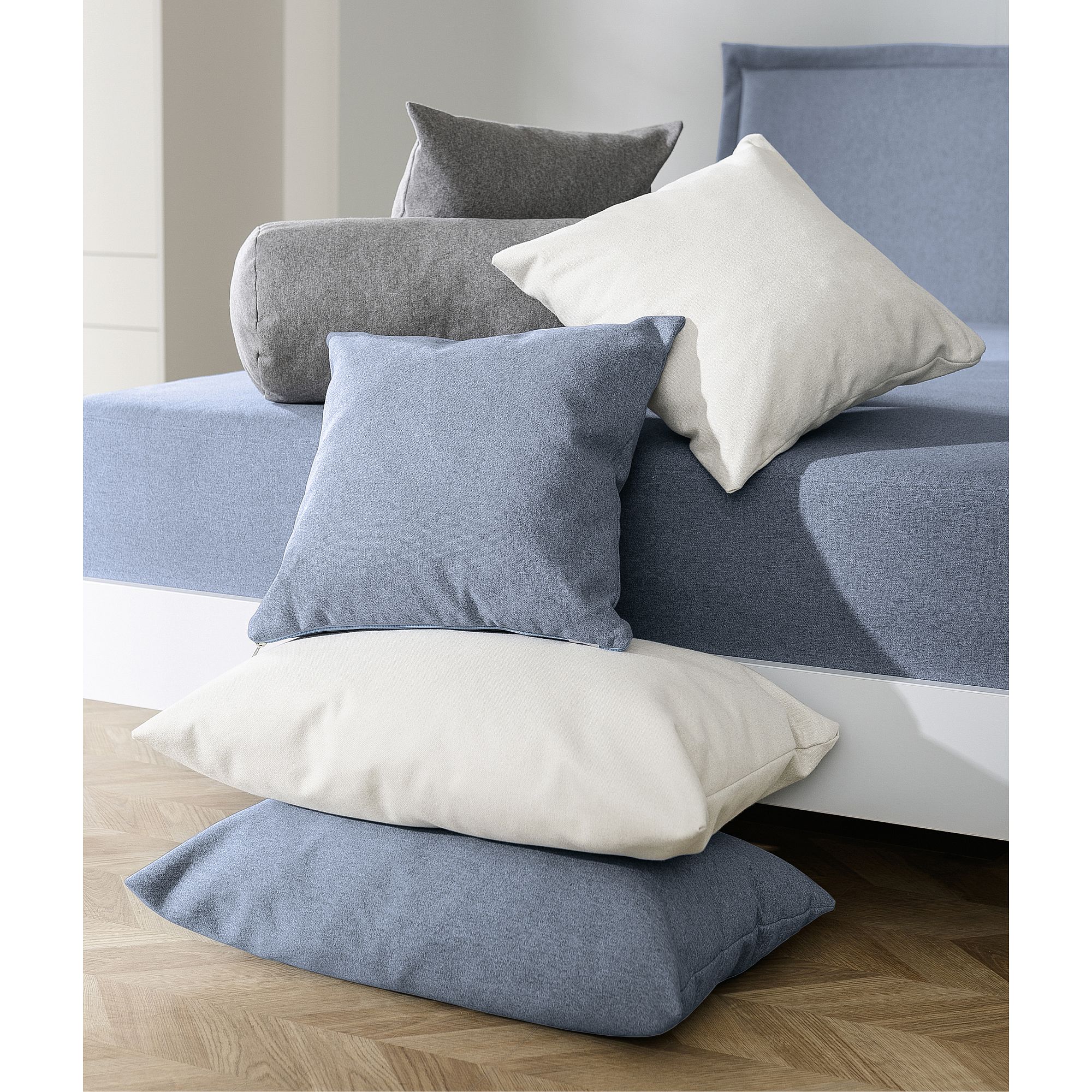 Gray and white pillows arranged on and beside a blue-sheeted bed.