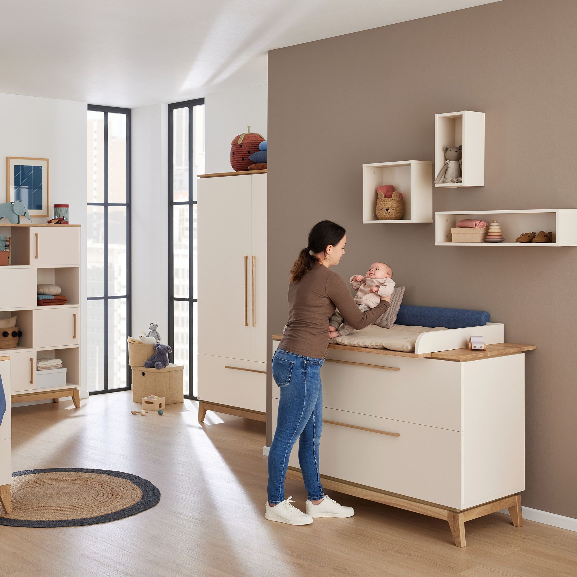 Frau wickelt ein Baby auf einem Wickeltisch in einem modernen, sonnendurchfluteten Kinderzimmer.