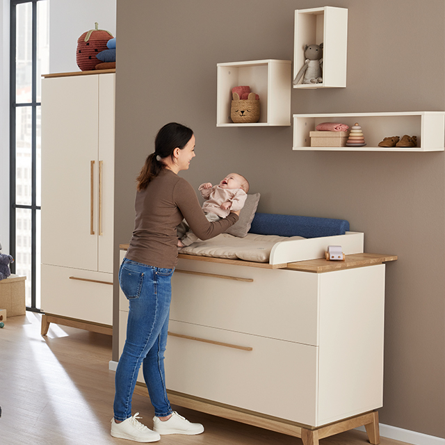 Woman changing a baby on a changing table in a modern nursery room.