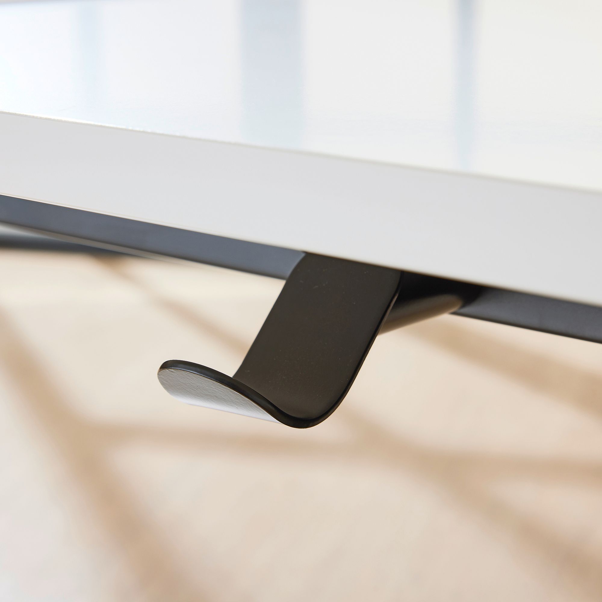 Nahaufnahme eines schwarzen Metallhakens, der unter einem weißen Schreibtisch angebracht ist.