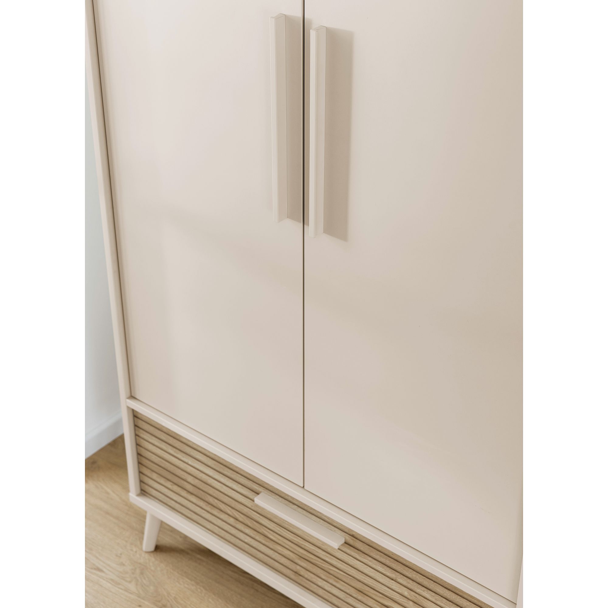 Beigefarbener Kleiderschrank mit zwei Türen und einer unteren Schublade auf einem Holzboden.