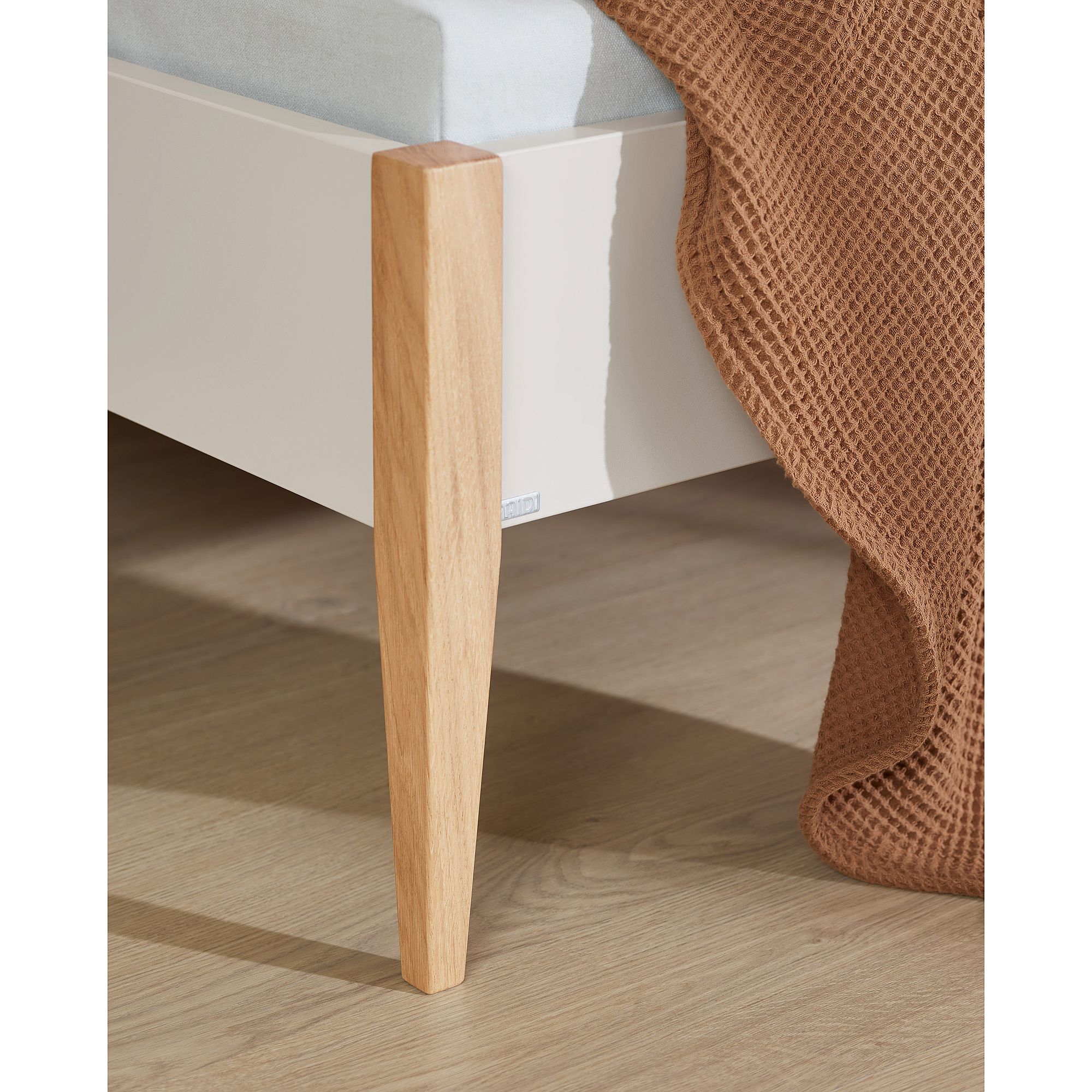 Nahaufnahme eines hölzernen Bettbeins in der Nähe einer strukturierten braunen Decke auf einem Holzboden.