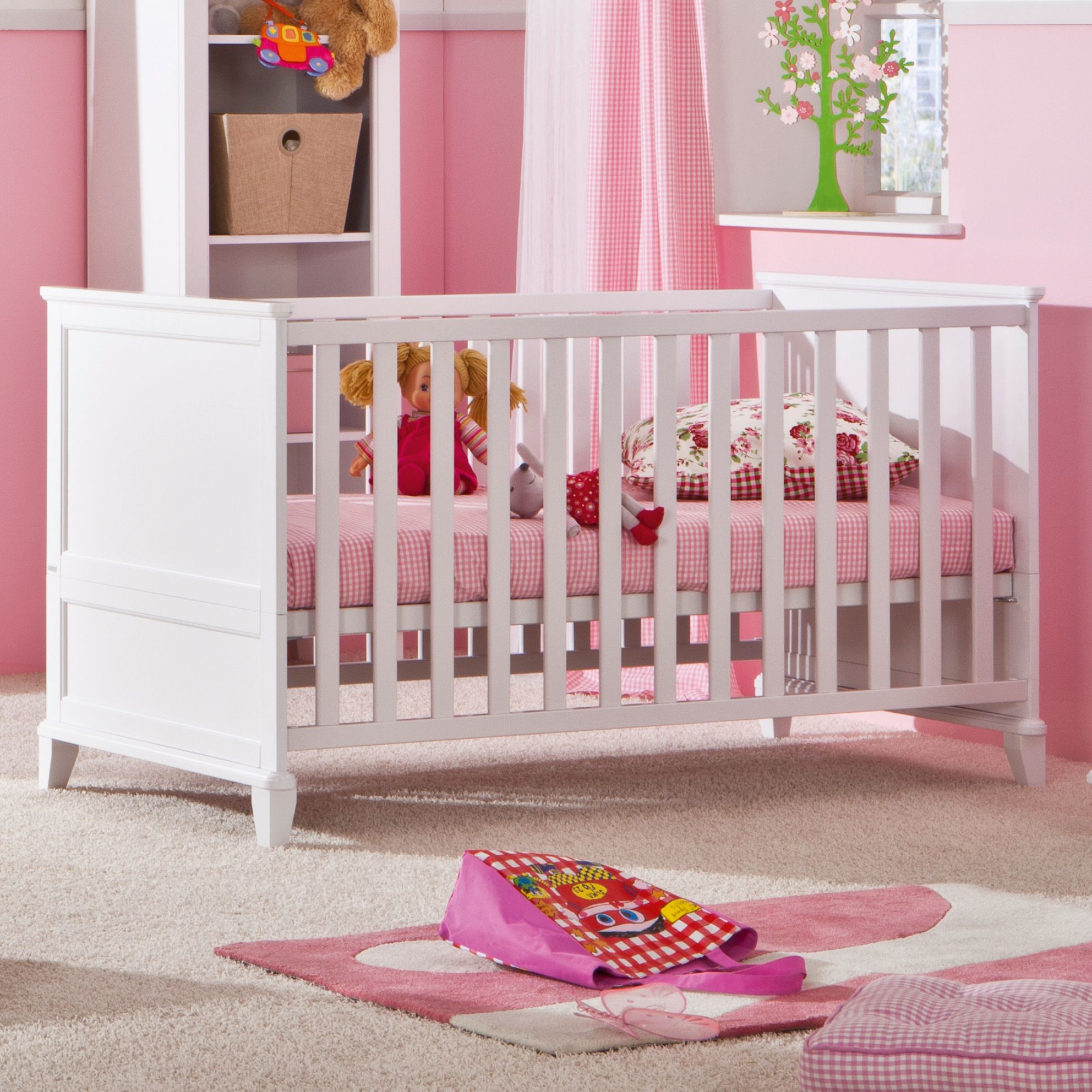 White crib with toys and pink bedding in a nursery with a soft pink decor.