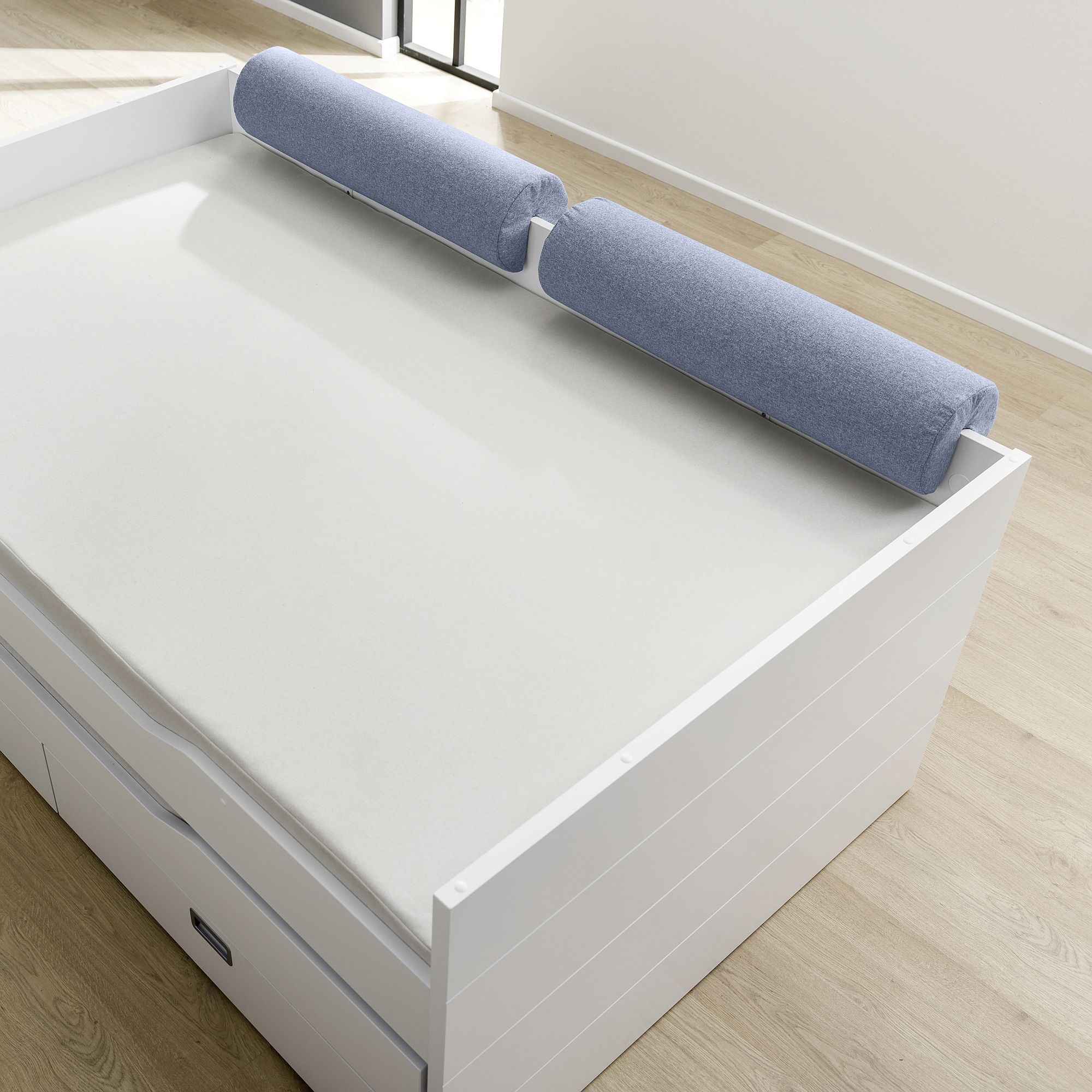 White bed with two long blue cylindrical pillows at the headboard.
