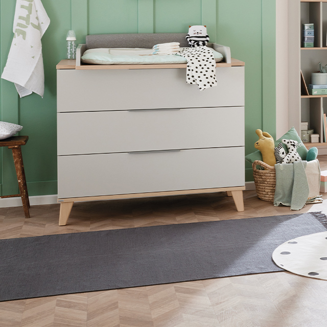 Modern baby changing table with drawers in a nursery with green paneled wall.