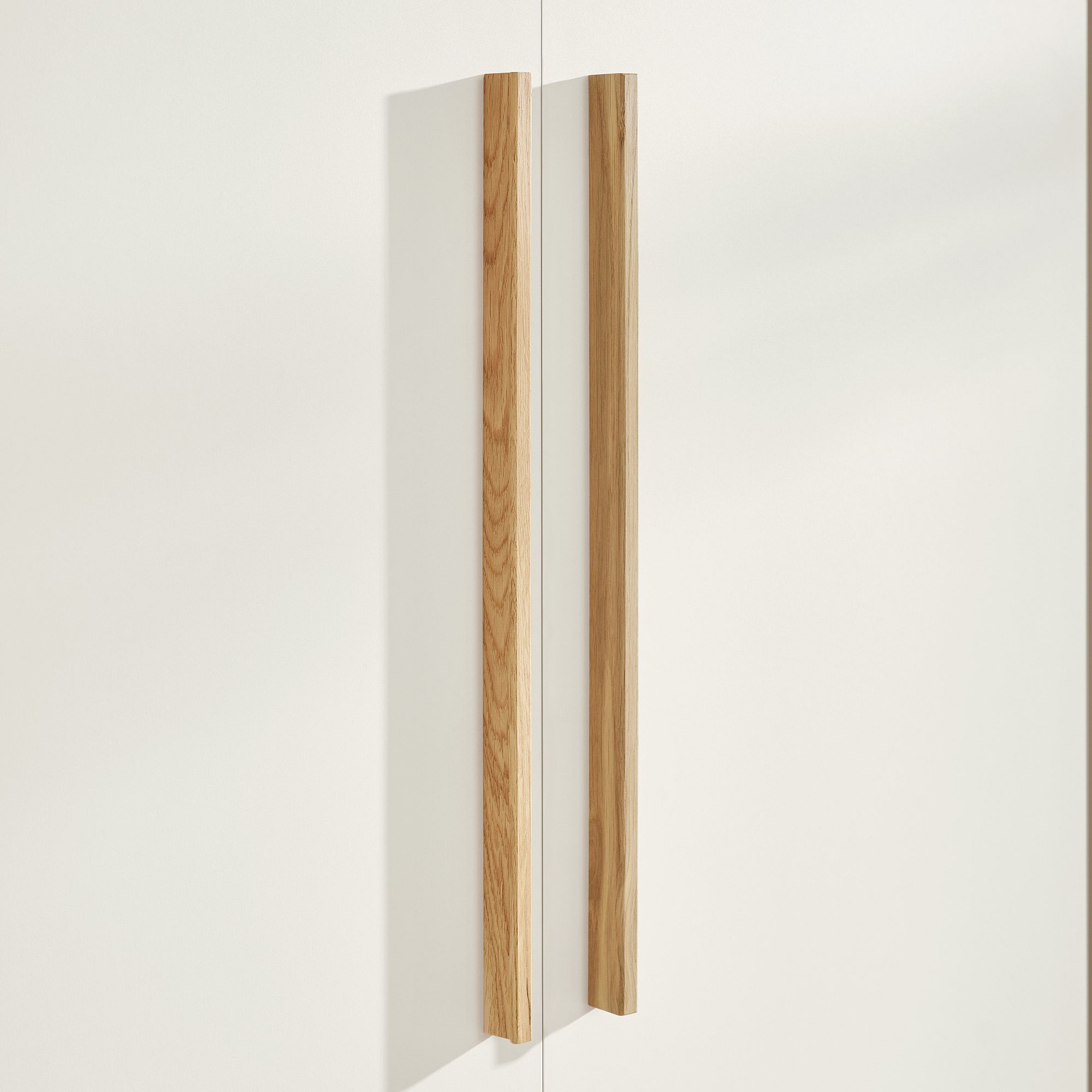 Zwei vertikale Holzgriffe an einer weißen Schranktür.
