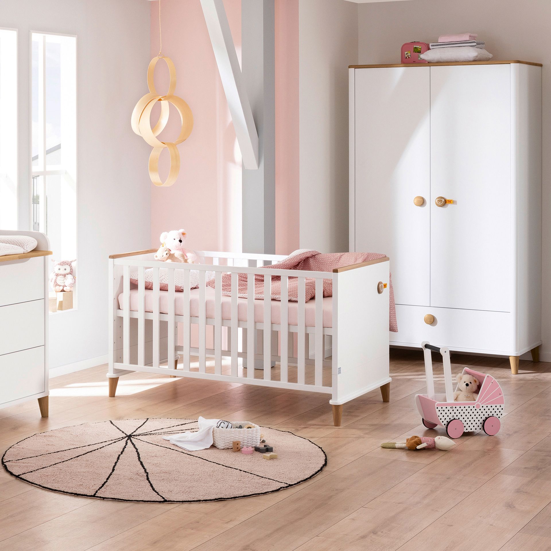 Ein modernes Kinderzimmer mit einem weißen Kinderbett, einem Kleiderschrank und rosa Akzenten.