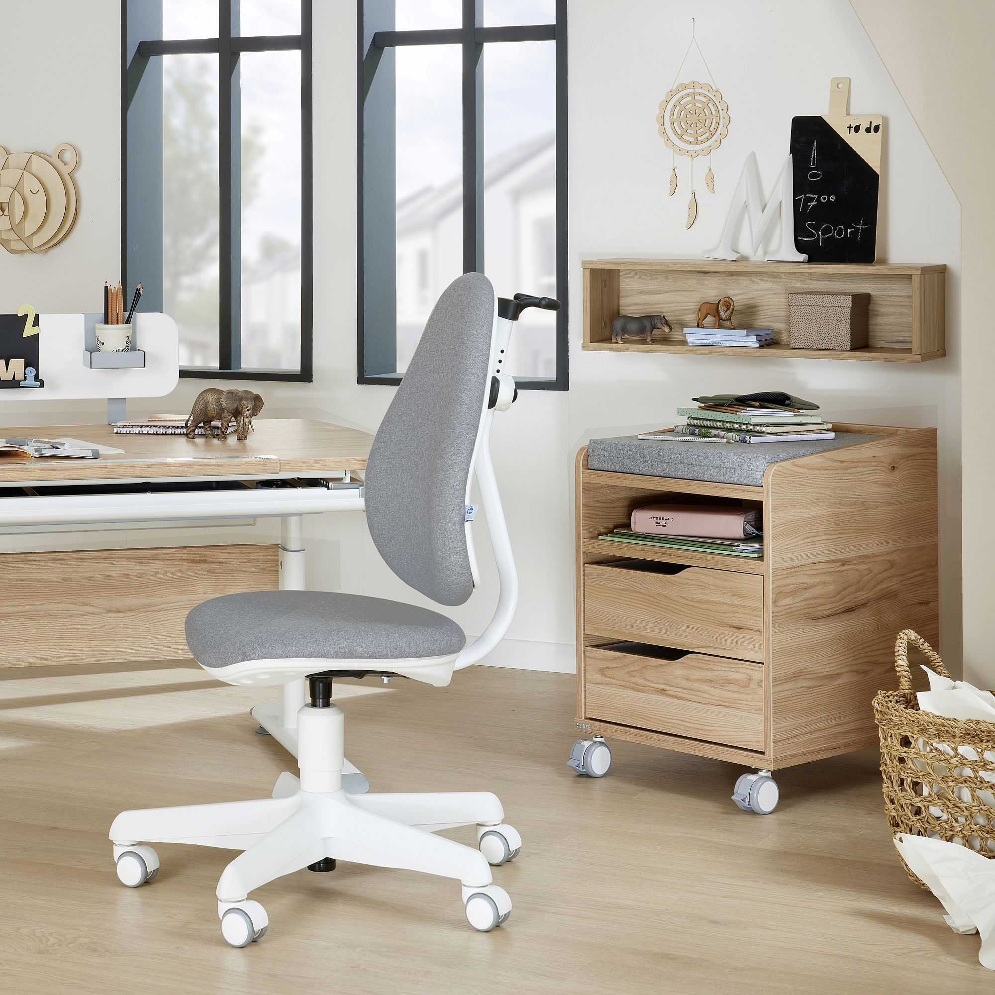 Modern home office with a grey chair, wooden desk, and shelves by the window.