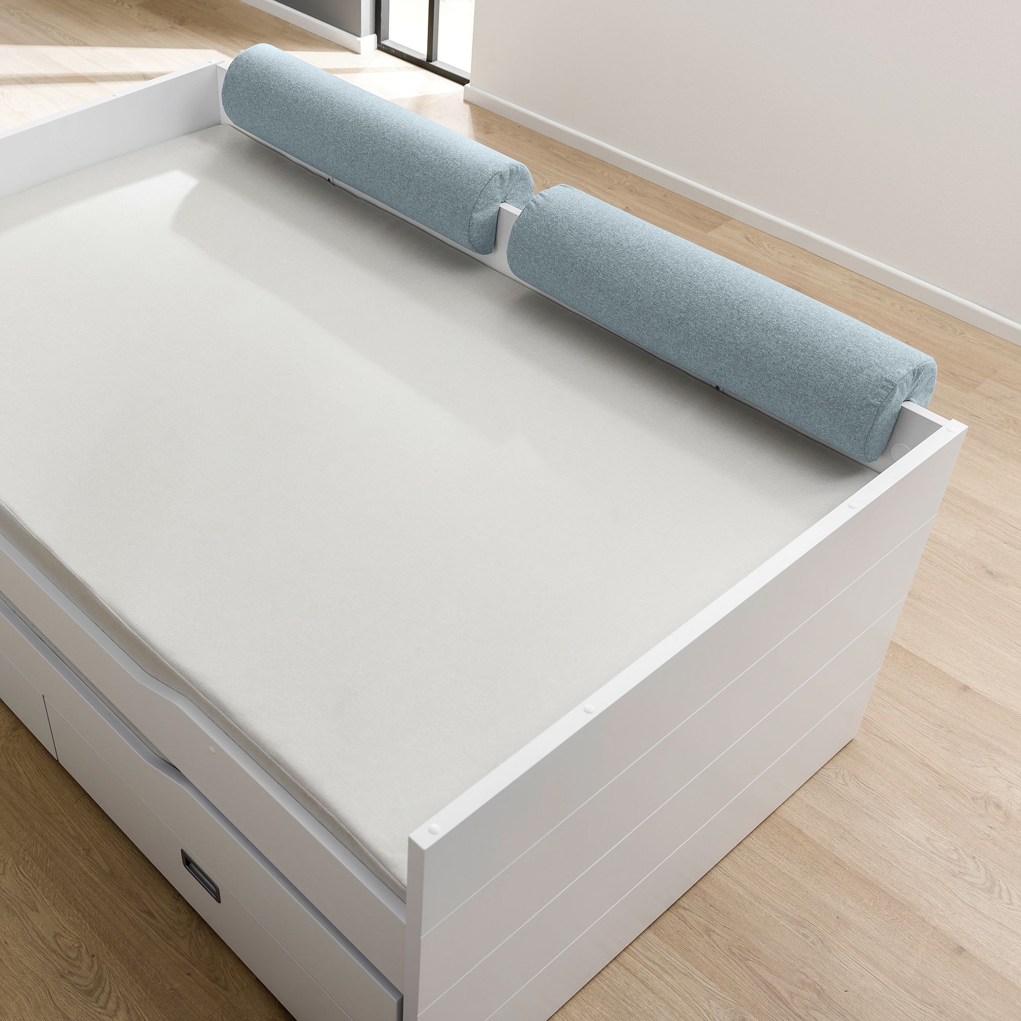 Light blue foam bed rail on a white single bed in a bright, minimal room.
